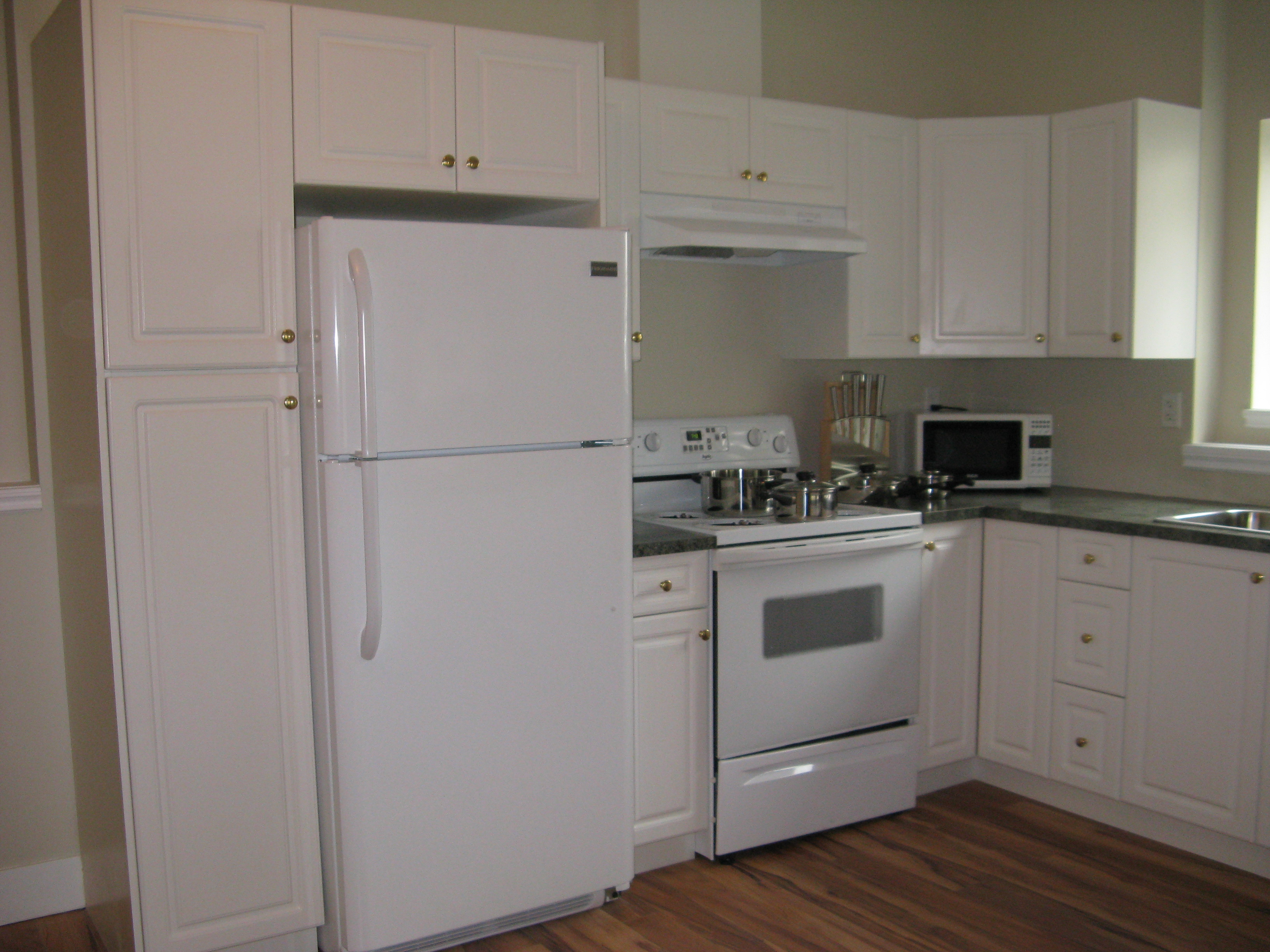 Bright lower-level secondary suite kitchen featuring clean white cabinets and full appliances