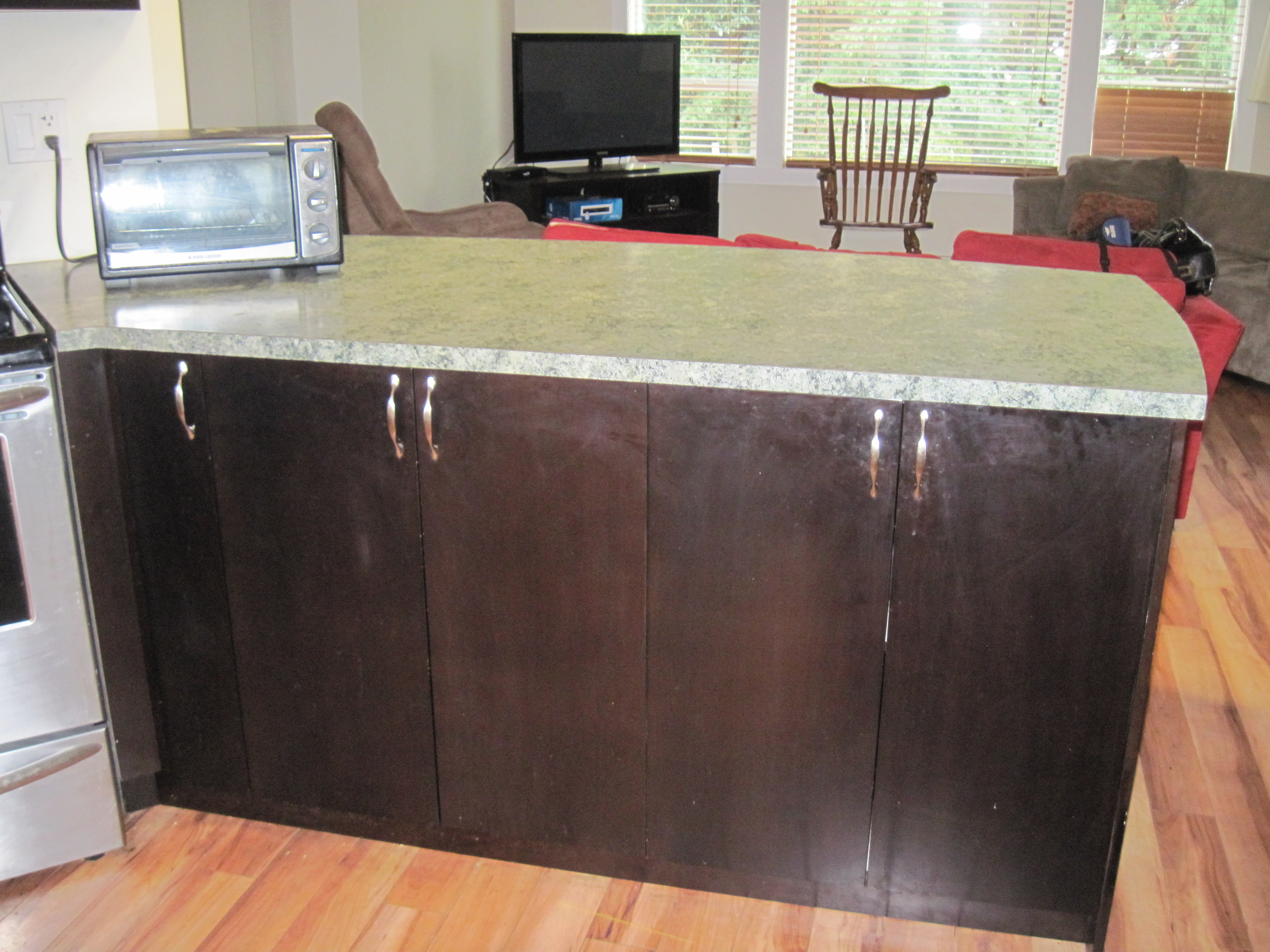 Kitchen with dark brown cabinetry, laminate countertops, and hardwood-style flooring looking into living area