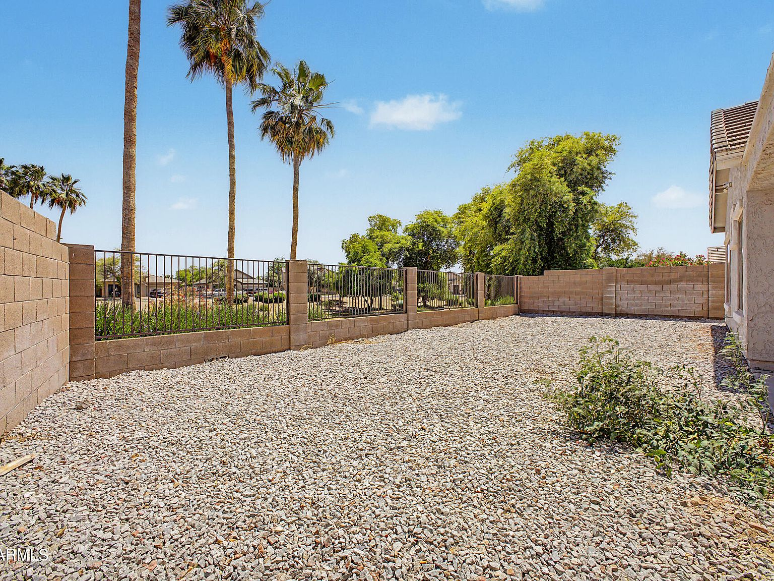 Backyard with low-maintenance gravel yard, cinder block wall, and wrought-iron view fence