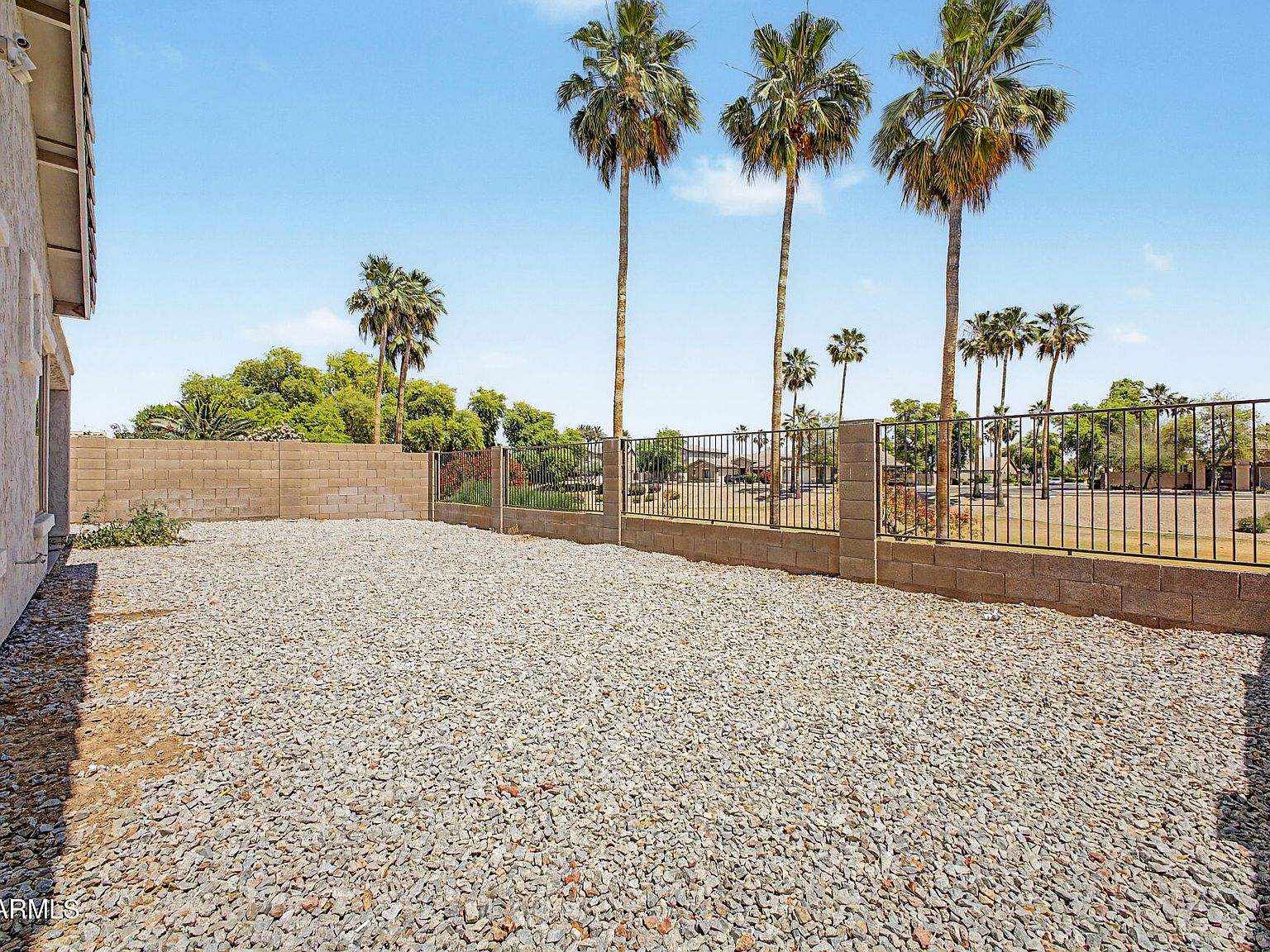 Backyard with gravel landscaping, cinder block wall, and iron fencing