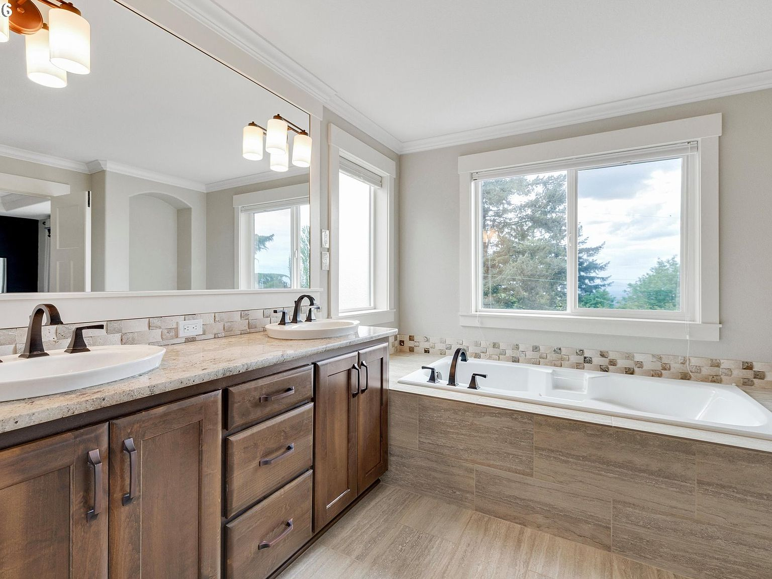 Ensuite primary bathroom with soaking tub, dark wood double vanity and large window lighting