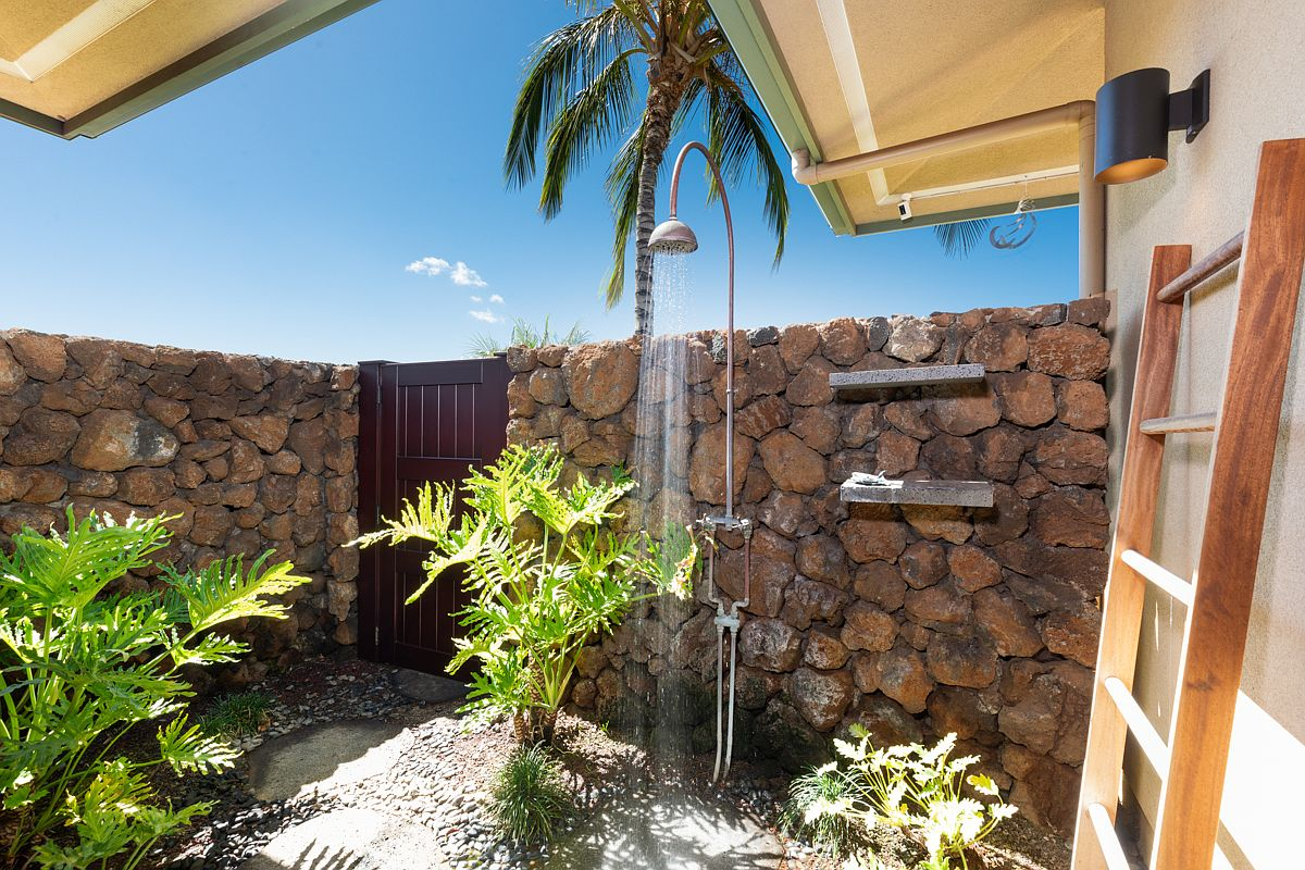Luxury outdoor shower courtyard built with privacy lava rock walls and accented by tropical palm and leafy landscaping.