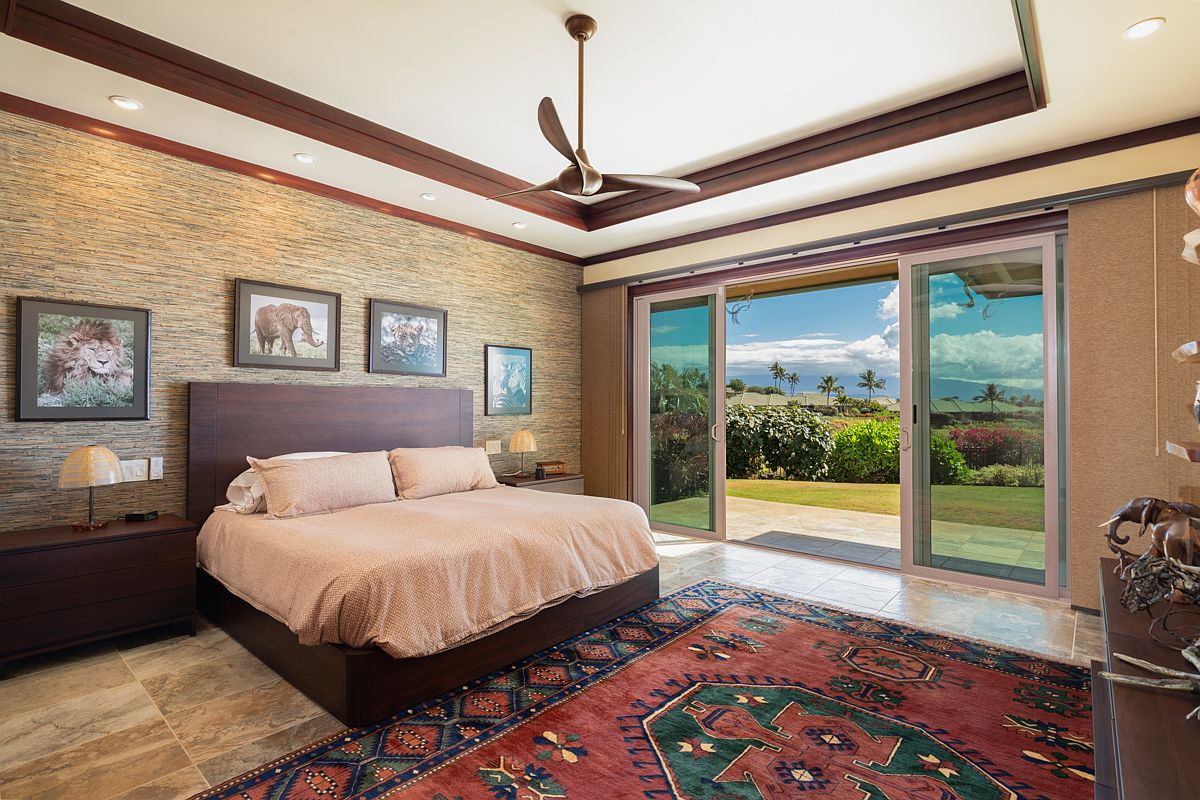 Main bedroom suite featuring a coffered ceiling with rich wood crown moldings, travertine tile floors, and a wide sliding pocket door to a grassy yard.