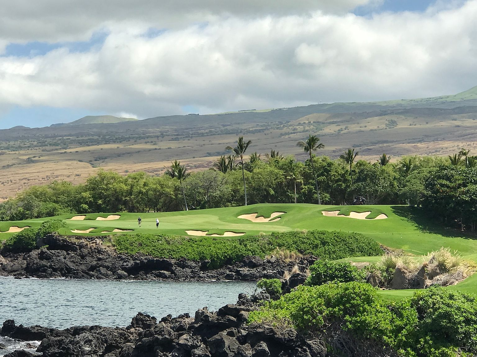 Oceanside golf course fairway with manicured green lawns and black basalt volcanic shorelines