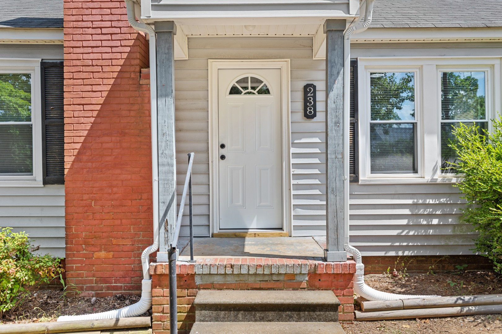 Charming covered front entrance porch with red brick foundation detailing