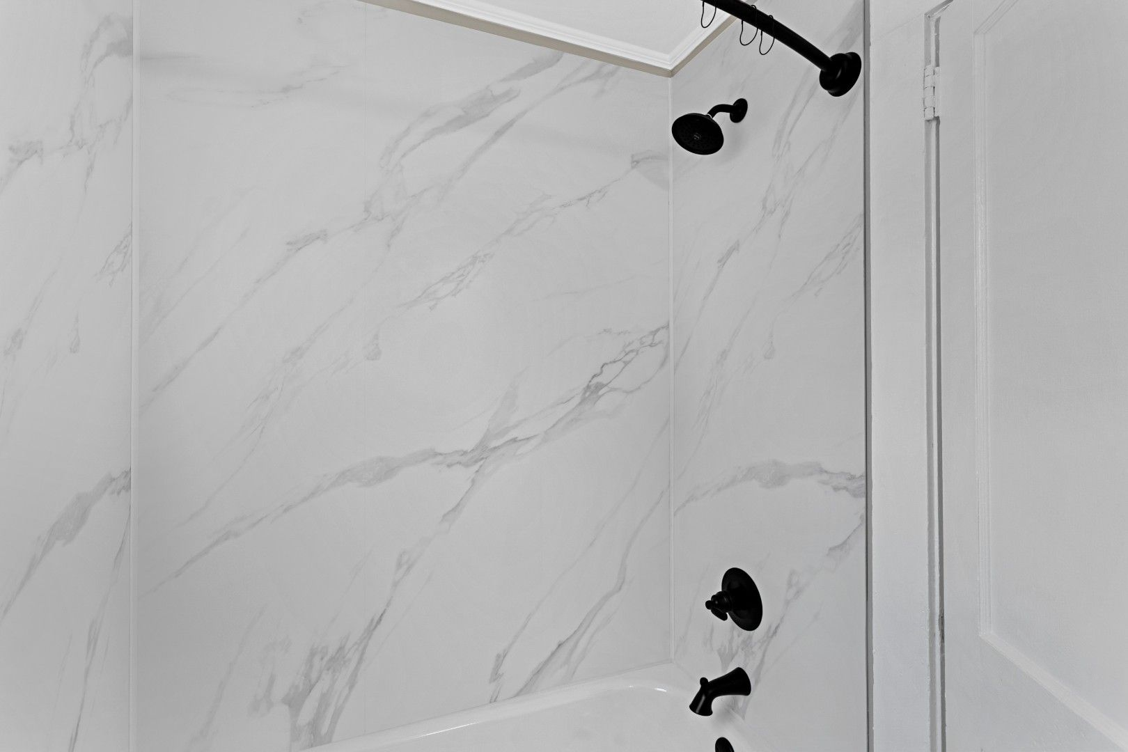 Close-up detail of the gorgeous faux marble bathtub tile surrounds and deep black shower fixtures