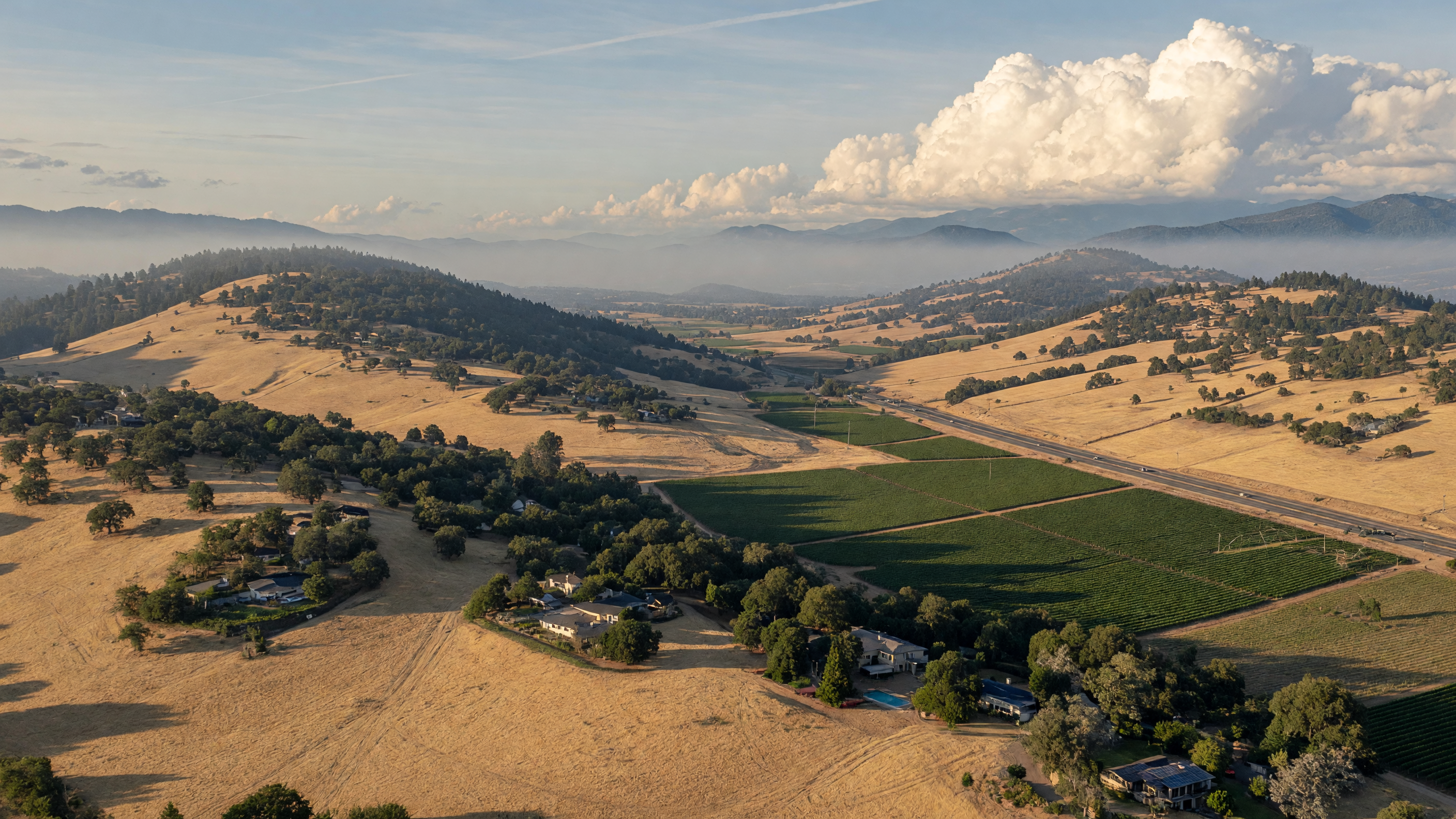 Golden dry grass hills and oak trees stretching across the Southern Oregon Rogue Valley, with a hazy mountain backdrop under summer skies