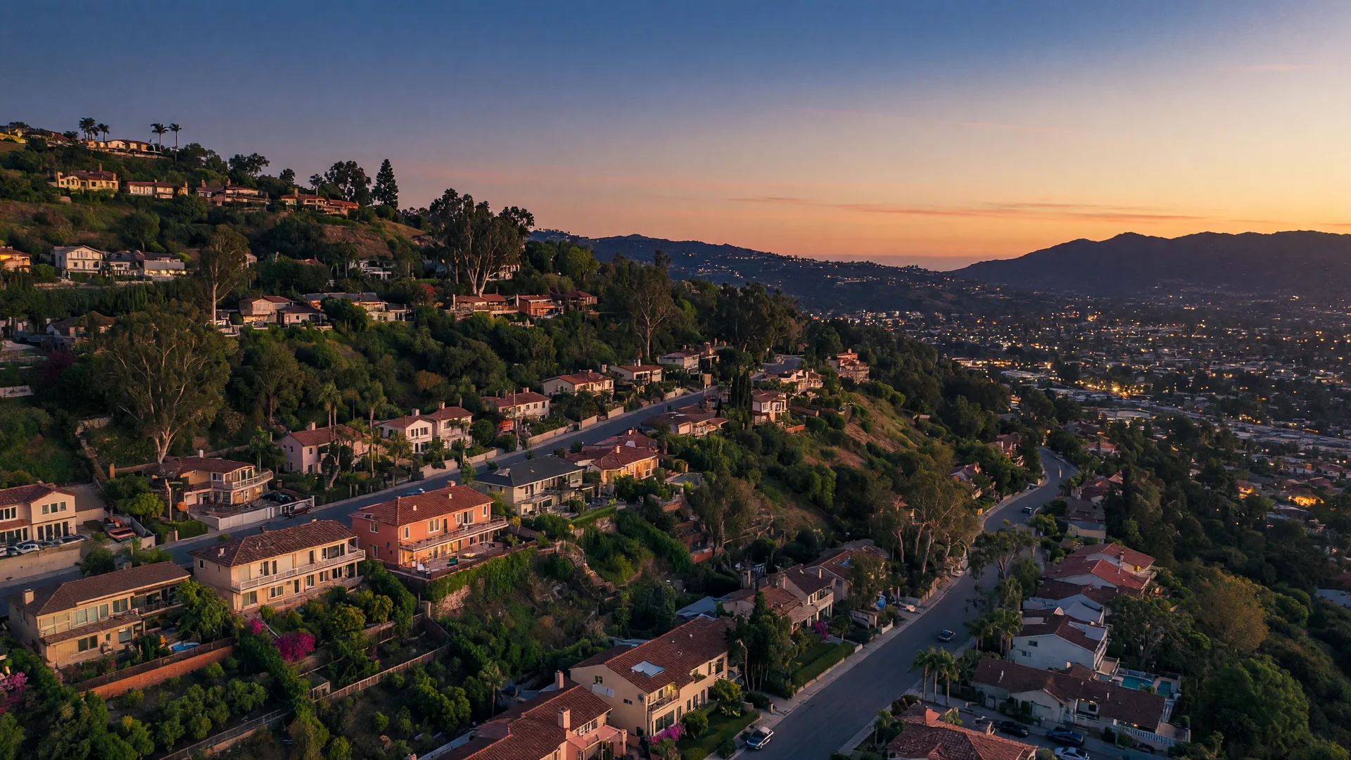 Summer golden-hour aerial view of Fullerton Hills hillside neighborhoods with winding tree-lined streets and distant mountain views