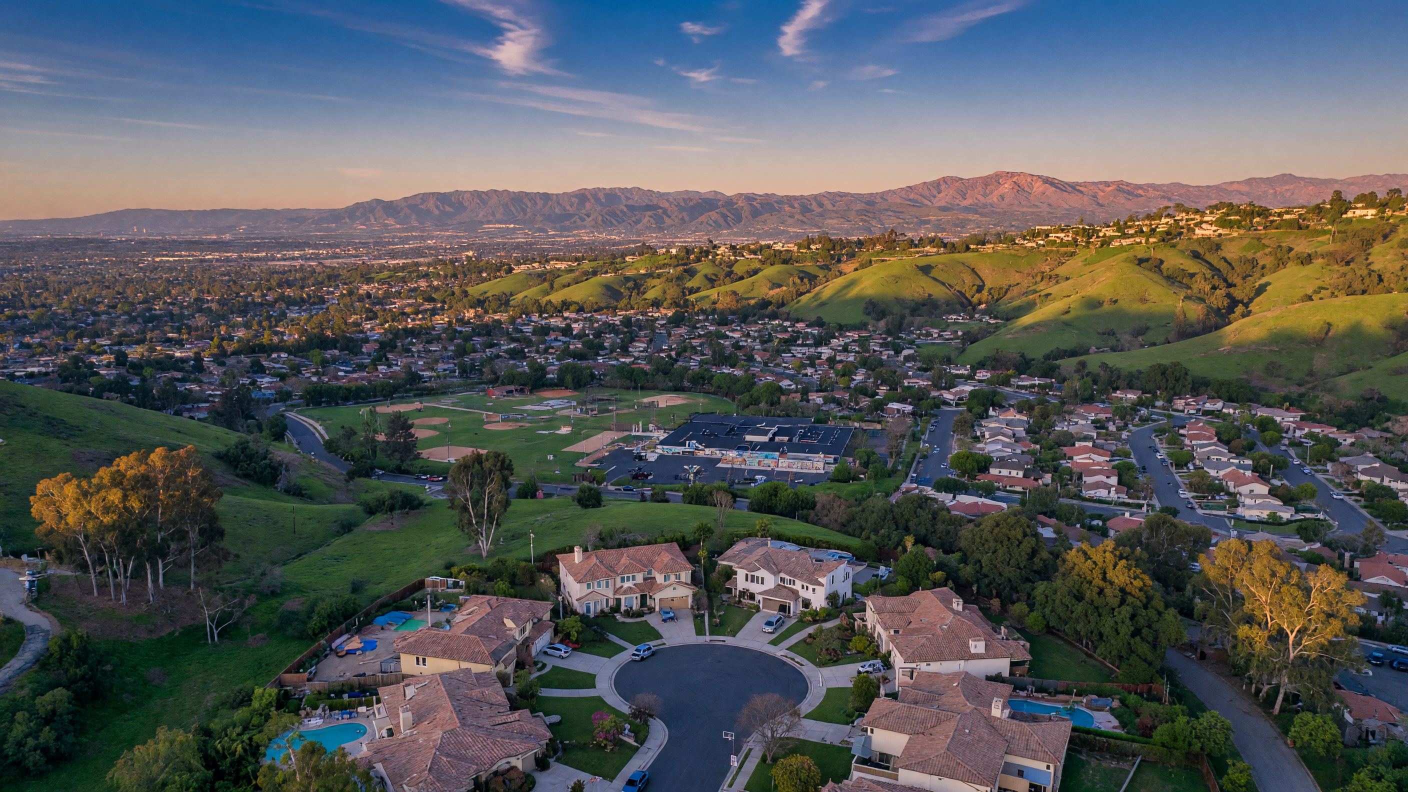 Aerial view of three hillside neighborhoods in North Fullerton — Raymond Hills, Sunny Hills, and Golden Hills — showing winding streets, mature trees, and mountain views