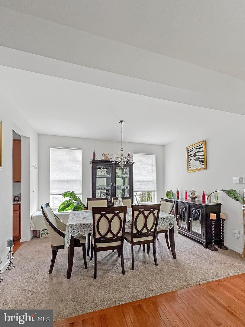 A bright formal dining room with carpeted floor, white walls, and triple windows admitting natural daylight