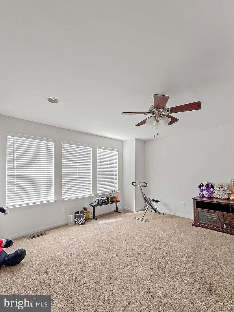 A bright, carpeted secondary bedroom featuring three tall windows on the upper floor