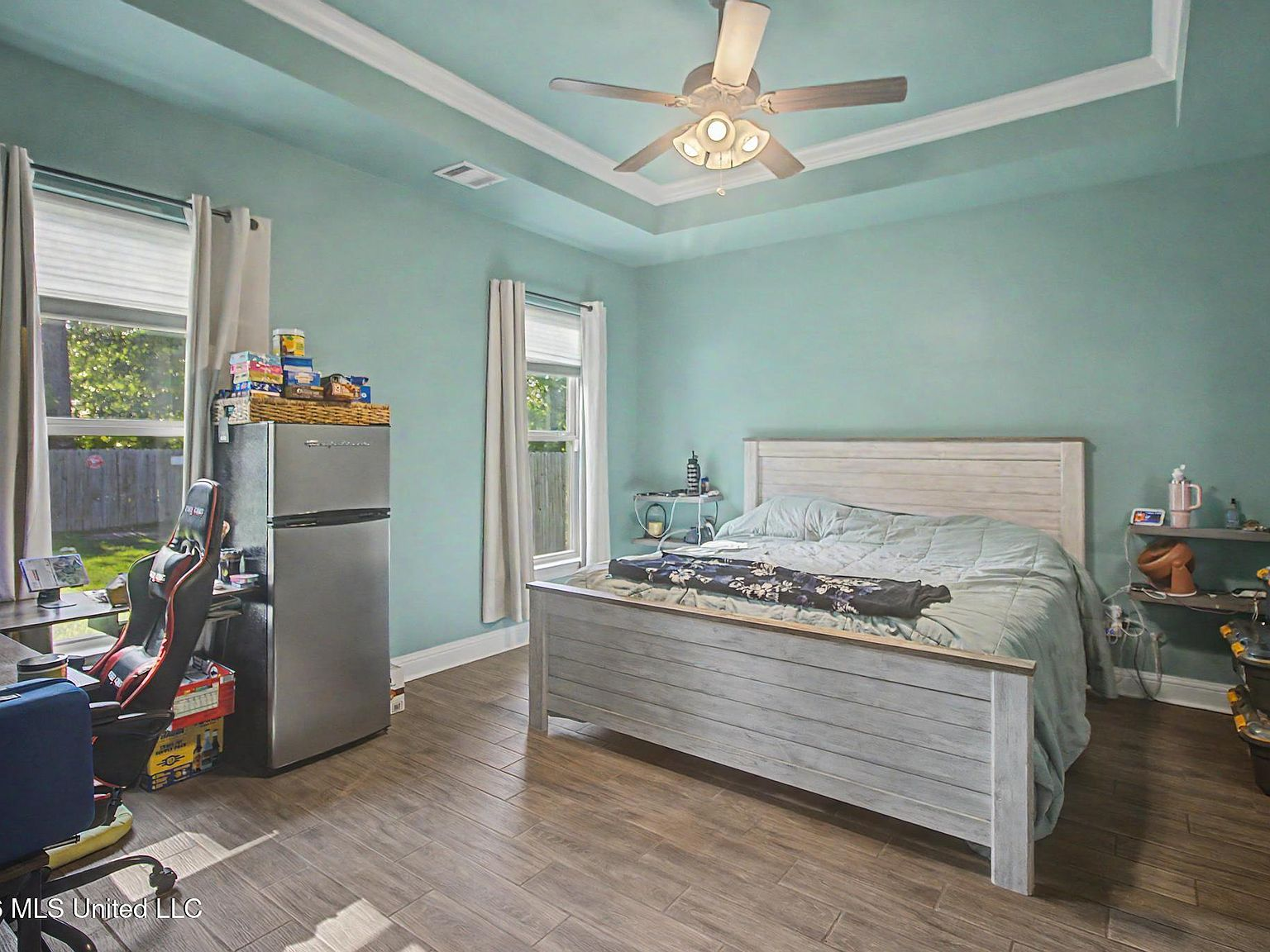 A calming primary suite showcasing deep tray ceilings and daylight streaming through twin windows