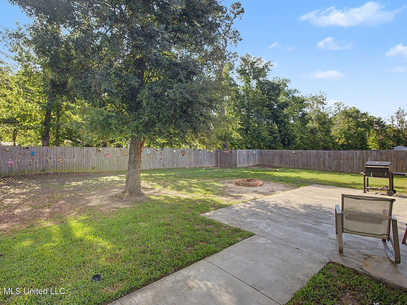 An inviting concrete rear patio overlooking a lush, peaceful backyard space bordered by tall pine trees