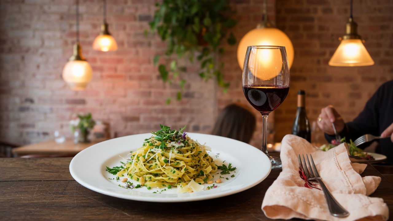 Elegant restaurant interior with warm pendant lighting, a beautifully plated dish on a wooden table, and a glass of wine