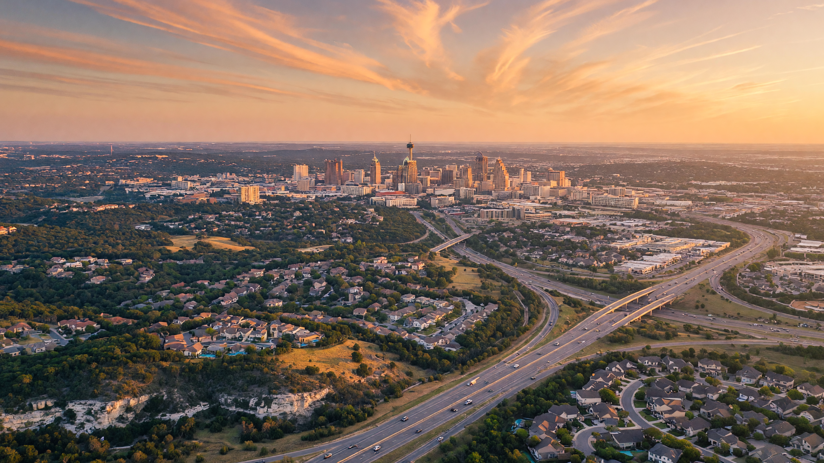 Panoramic view of the San Antonio skyline in the distance with Hill Country terrain and suburban development in the foreground, showing the connection between the growing metro region and the communities along the I-10 corridor