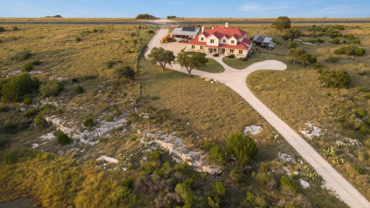 Aerial view of a Hill Country property on several acres with natural limestone terrain, scattered oak trees, and a long gravel driveway — beautiful but representative of the maintenance commitment that comes with rural acreage