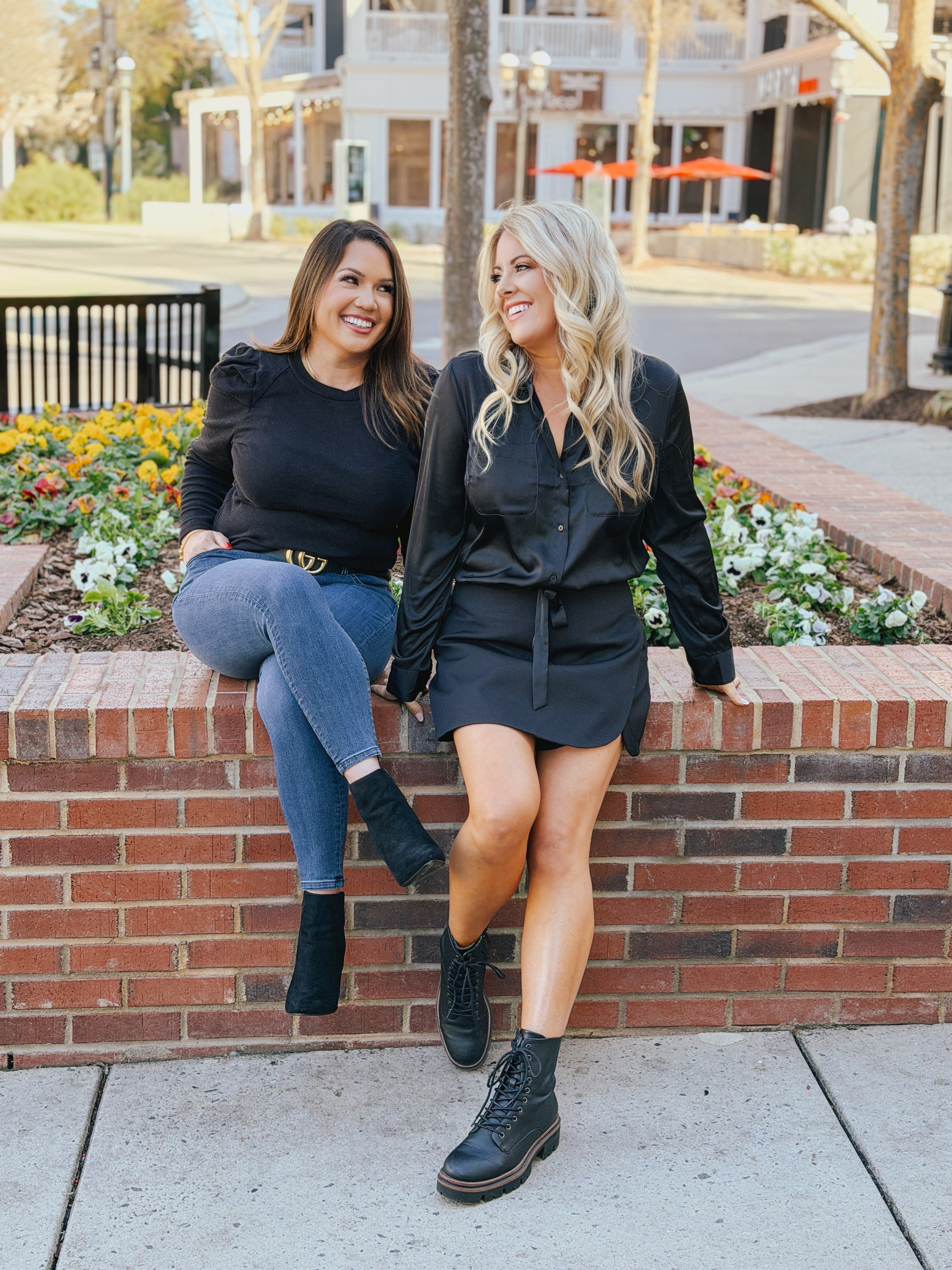 Tiffany Huntoon and Lauren Rocco sitting together on a decorative brick wall in an outdoor shopping area, smiling at each other