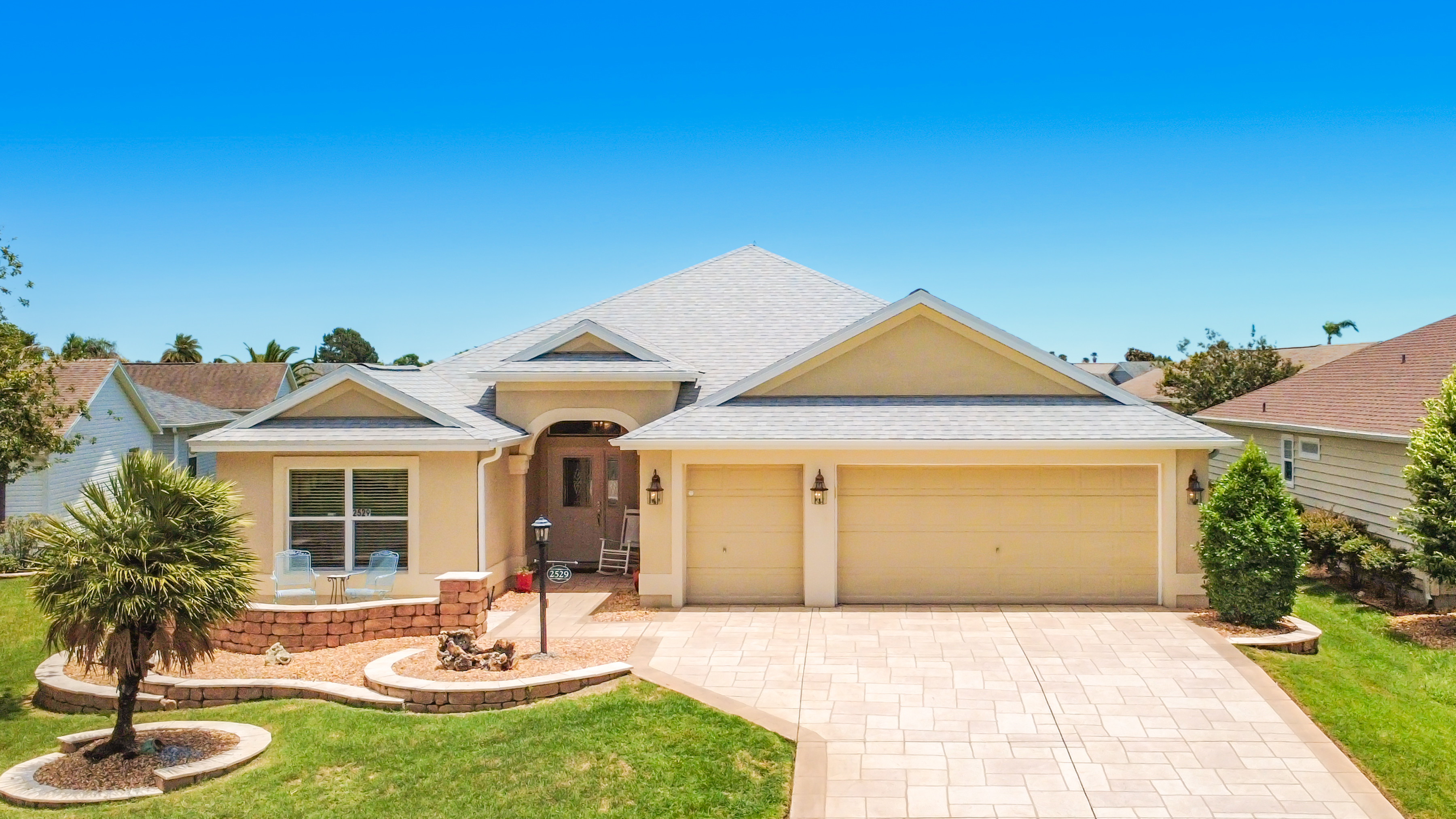 Front exterior of 2529 Edenville Path showing cream stucco facade, stone paver driveway, and landscaped front yard in The Villages FL