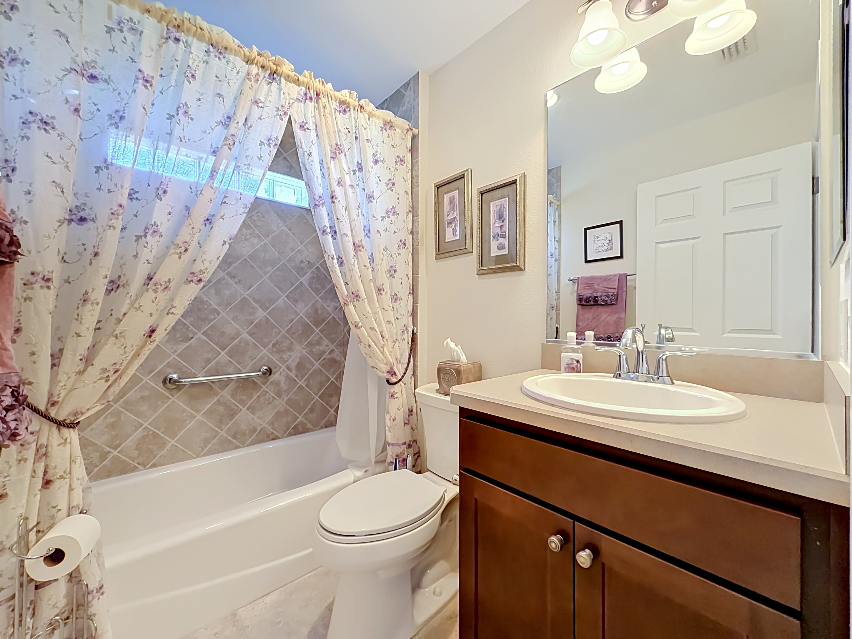 Bathroom with dark vanity, dual sinks, and tiled walk-in shower with mosaic accent band