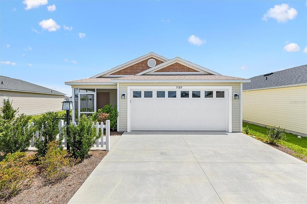 Front exterior of 7185 Fay Ct, a Topaz patio villa in The Villages, FL with white picket fence and two-car garage