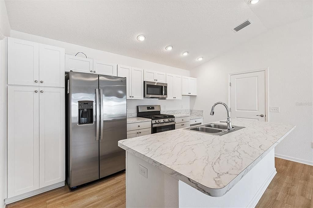 Full kitchen view showing oversized island, white cabinetry, marble-look countertops, and stainless steel refrigerator at 7185 Fay Ct