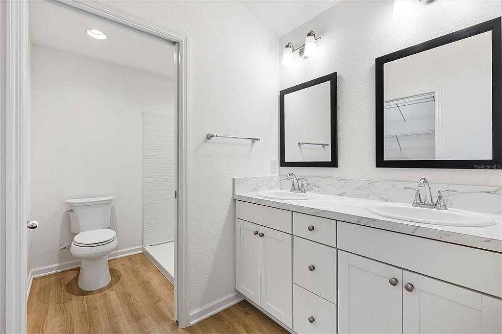 Primary bathroom with dual vanities, white shaker cabinetry, black-framed mirrors, and modern finishes