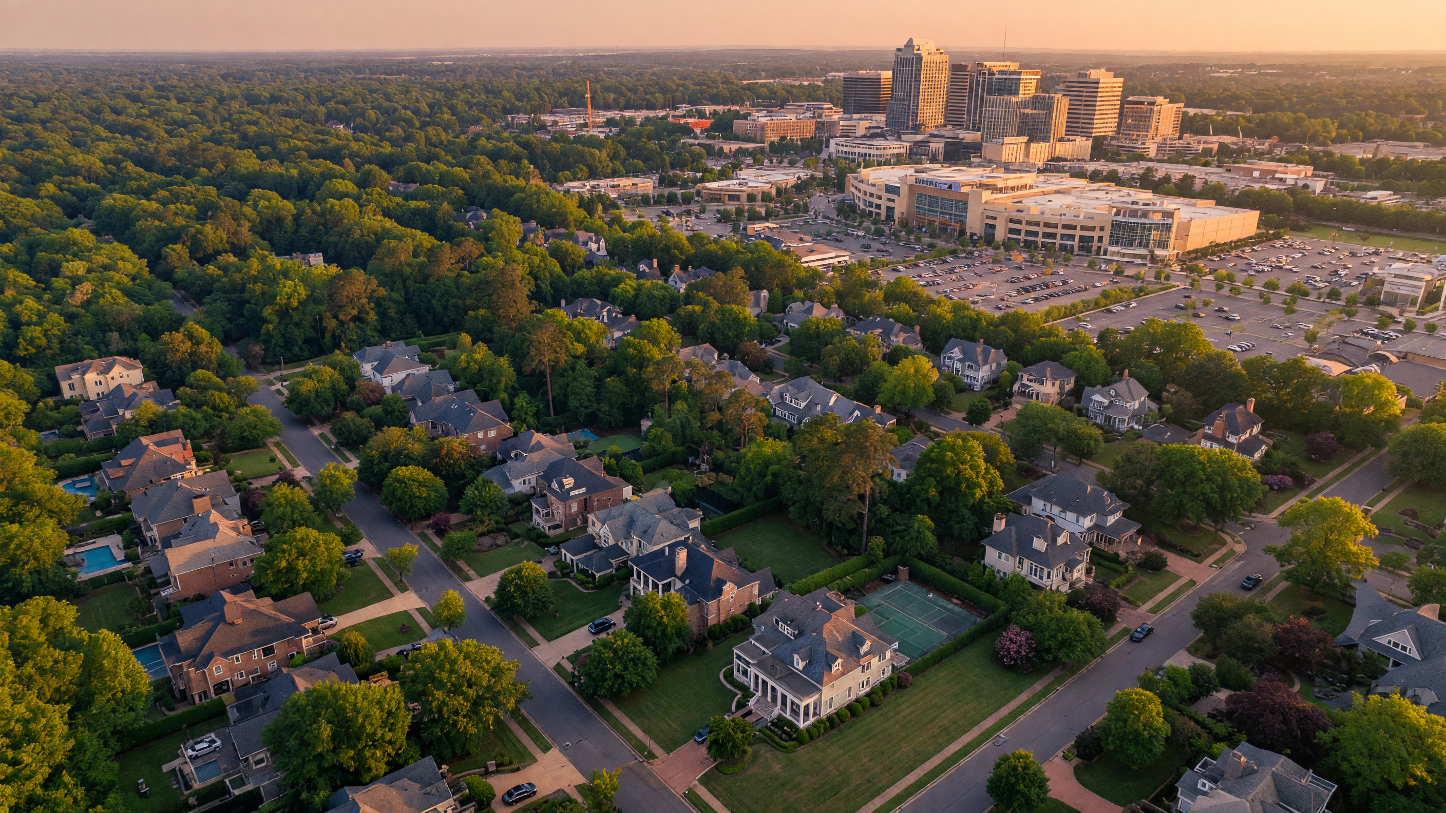 Aerial view of SouthPark Charlotte NC at golden hour showing tree-lined streets, luxury homes, and the SouthPark shopping district in the distance