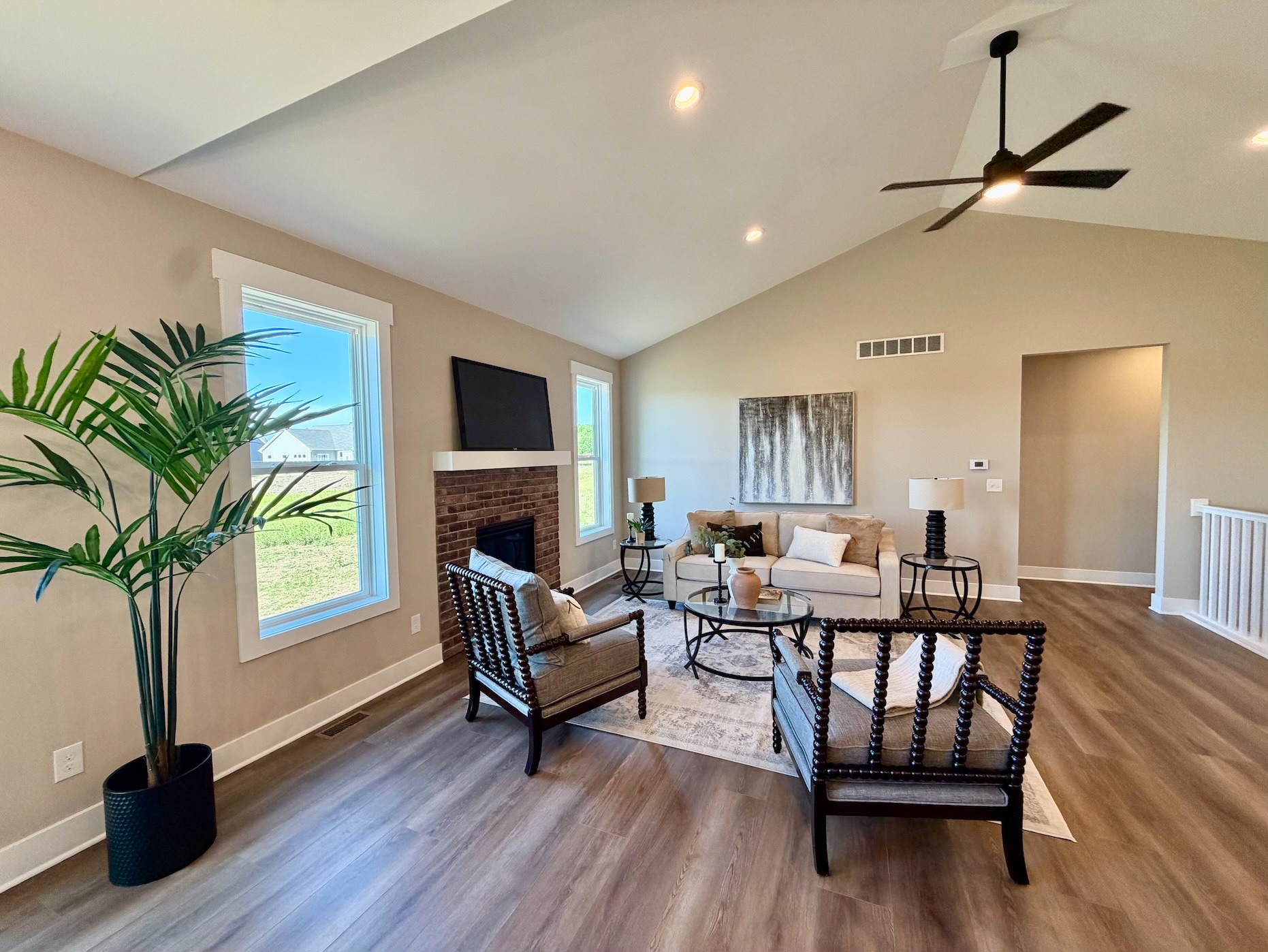 Staged vaulted great room with sofa, accent chairs, and brick fireplace