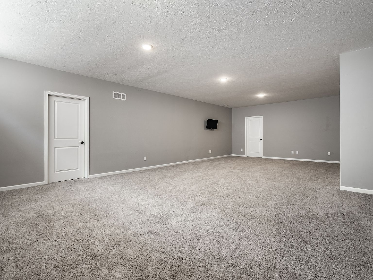 Finished basement recreation room with gray walls and carpeting