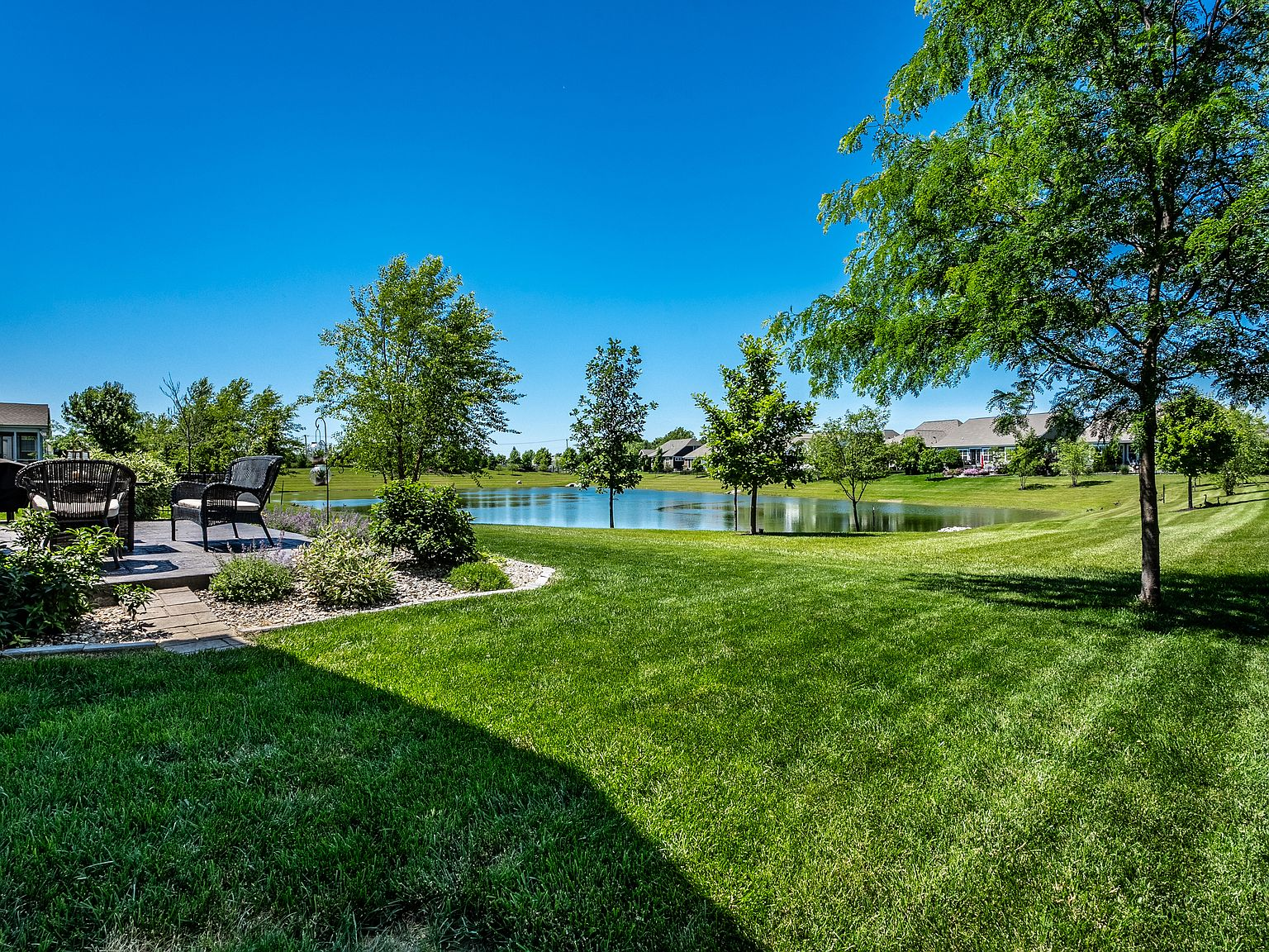 Backyard view overlooking the community pond with manicured lawn and mature trees