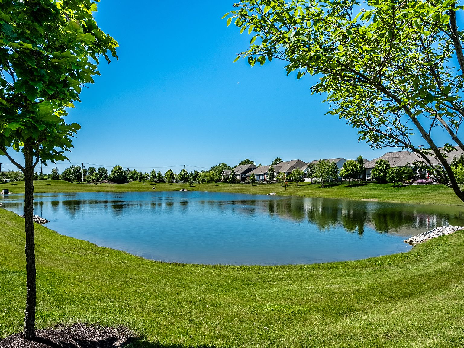 Wide view of the community pond from the backyard with lush green lawn and blue sky