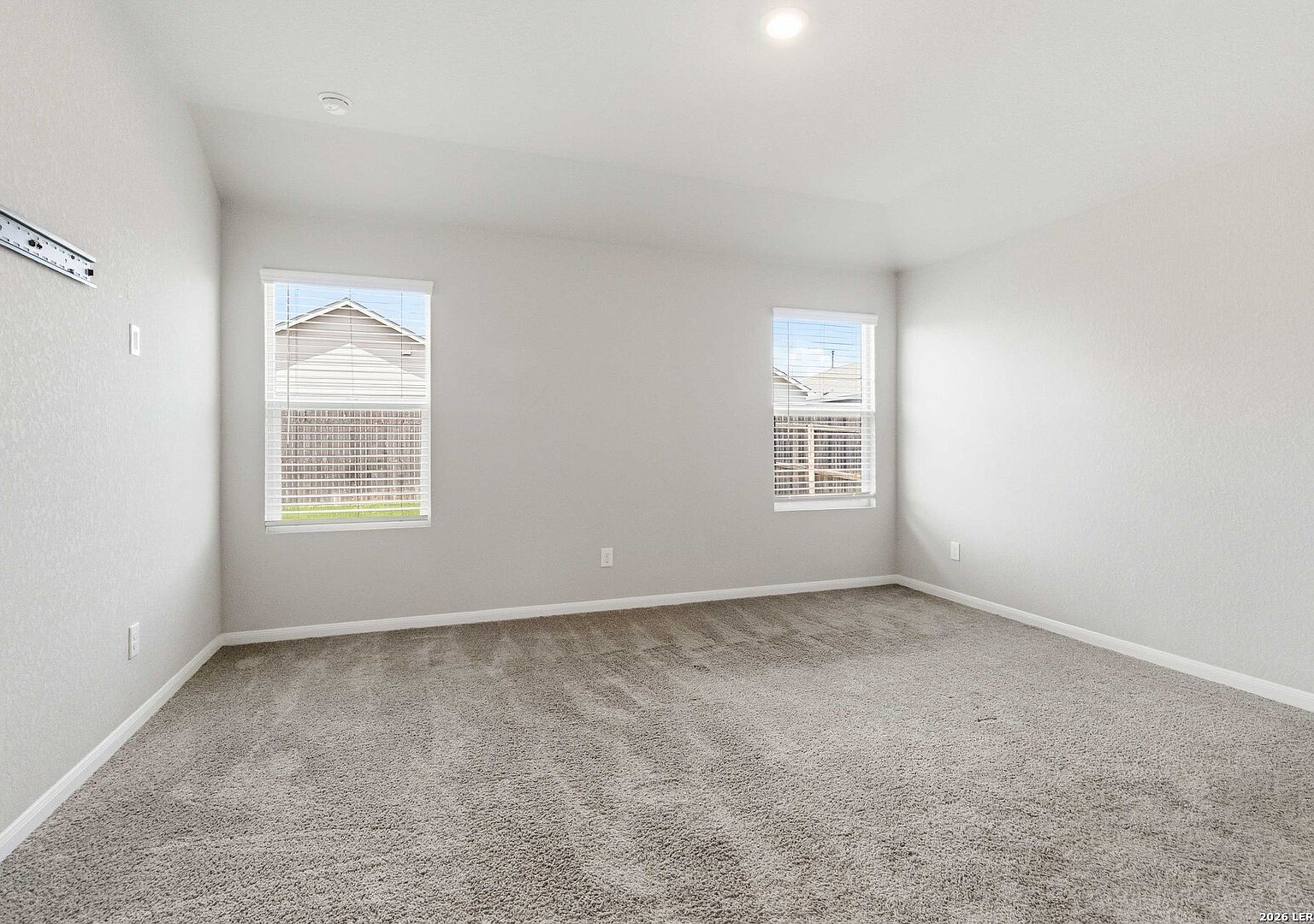 Primary bedroom with grey carpet and two windows with natural light