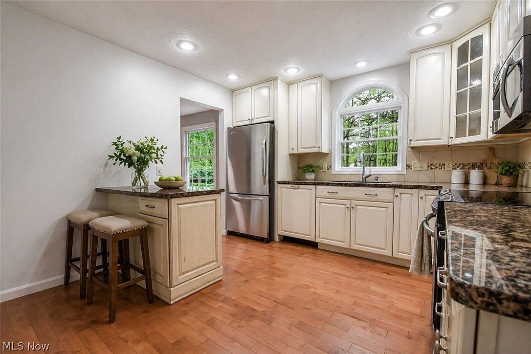 Kitchen with off-white cabinetry, dark granite countertops, and wood-toned flooring
