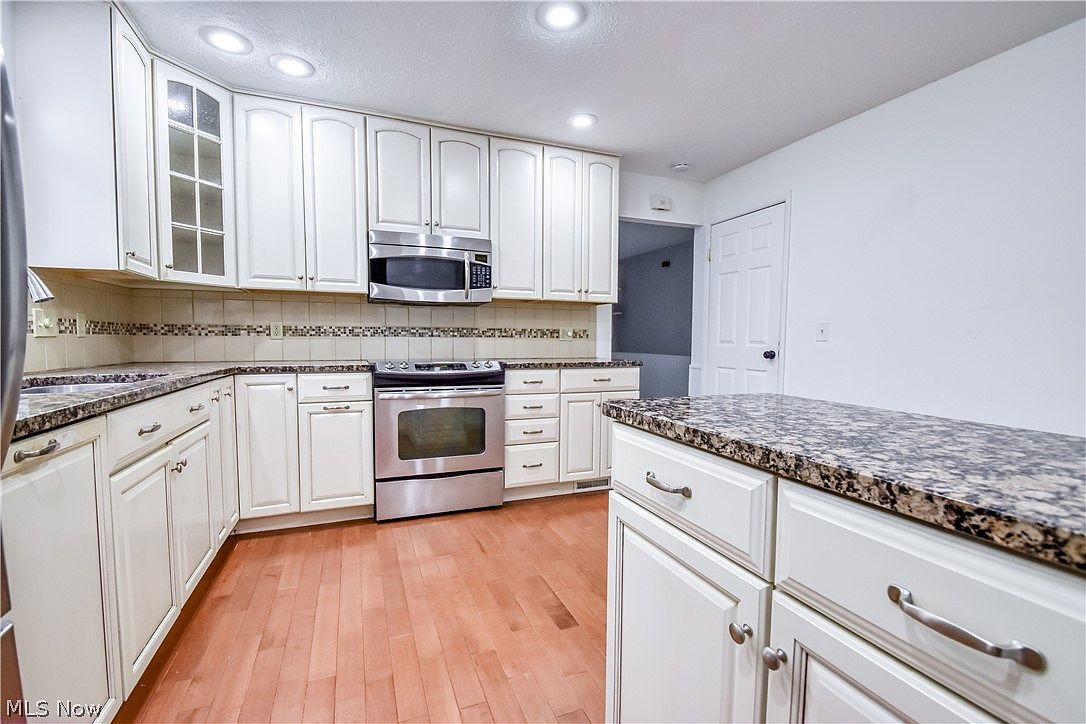 Kitchen with white cabinetry, granite countertops, and tile backsplash