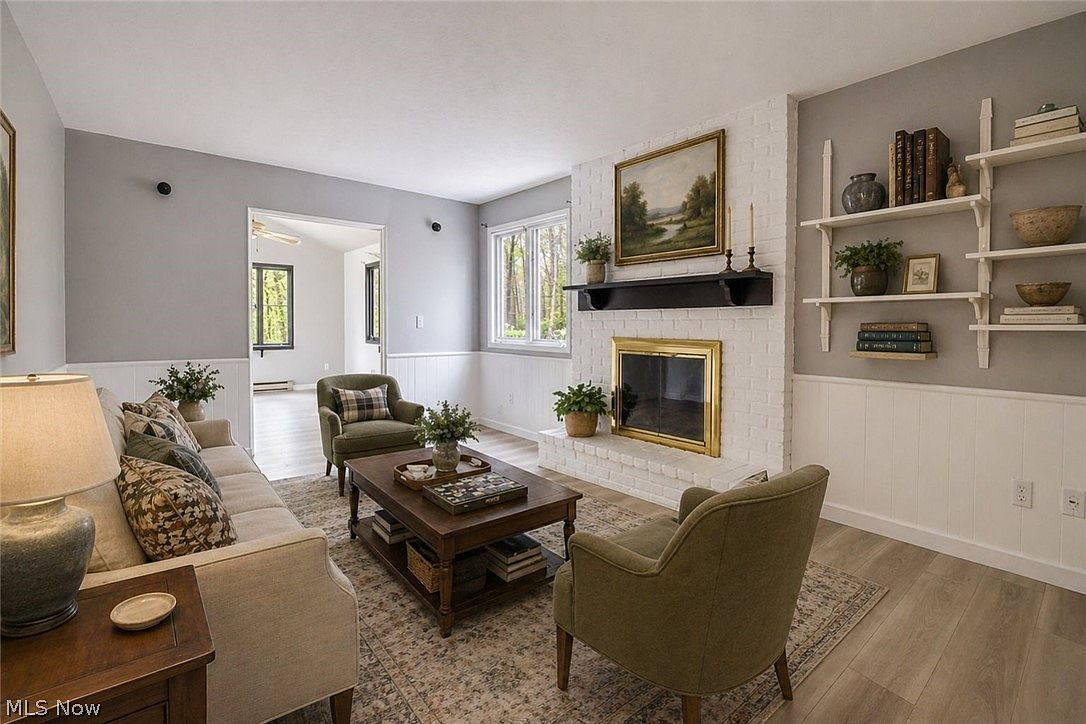 Living room with white brick fireplace, wainscoting, and natural light