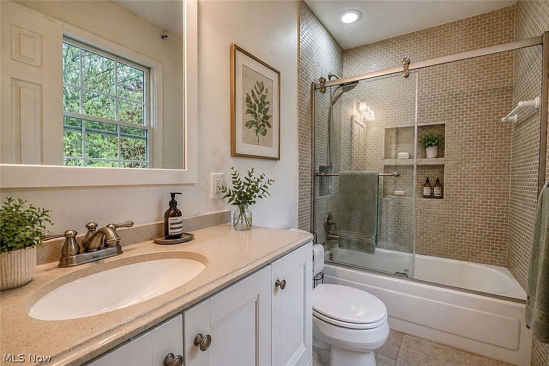 Bathroom with beige mosaic tile shower, neutral countertop, and oiled-bronze hardware