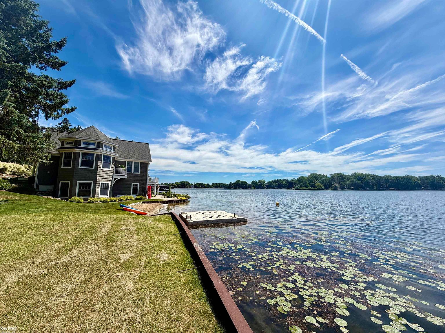 Backyard with lawn sloping to the lakefront, dock, and kayaks on shore