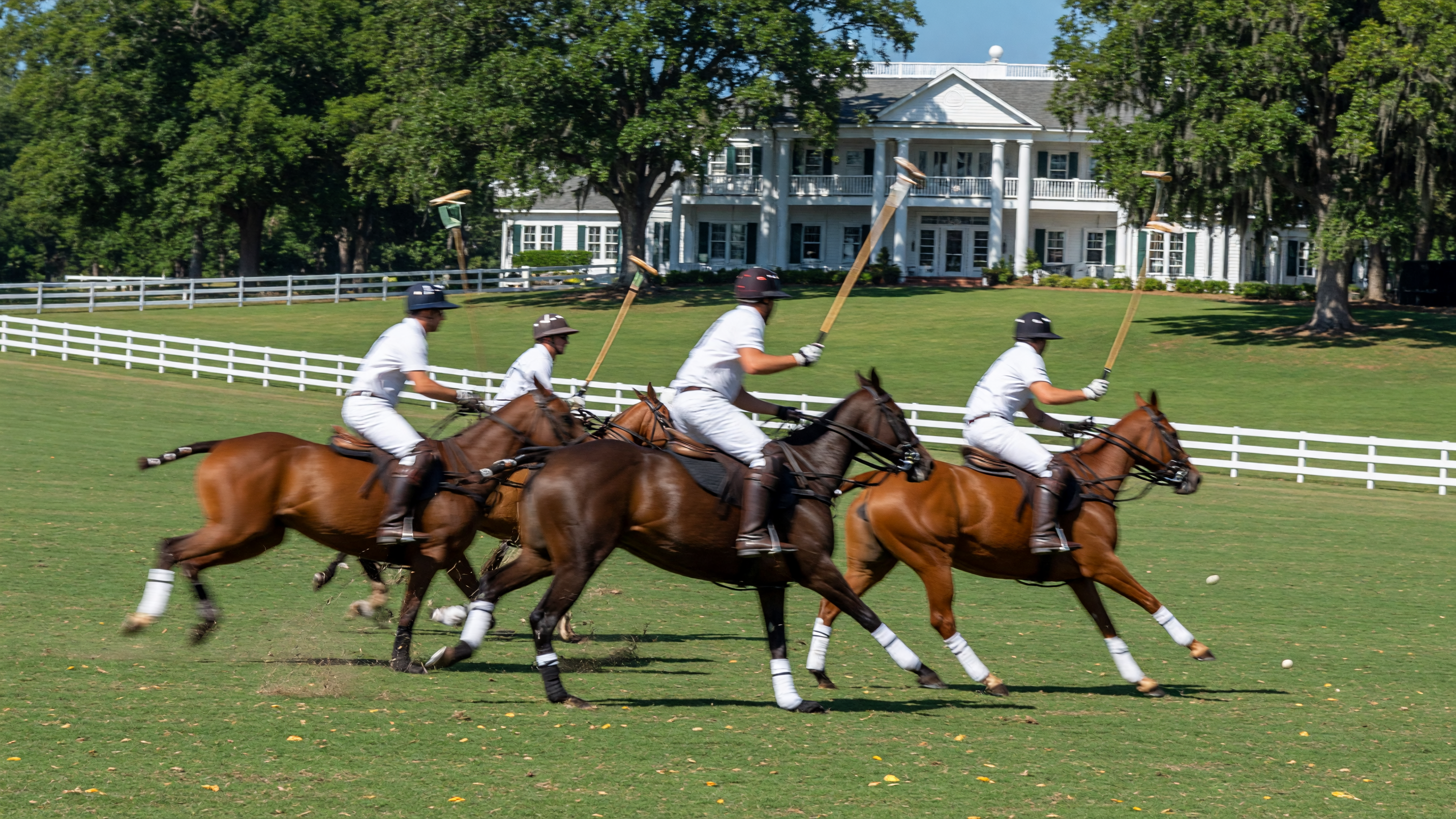 Polo match at New Bridge Polo & Country Club in Aiken, South Carolina with players on horseback and white clubhouse in background