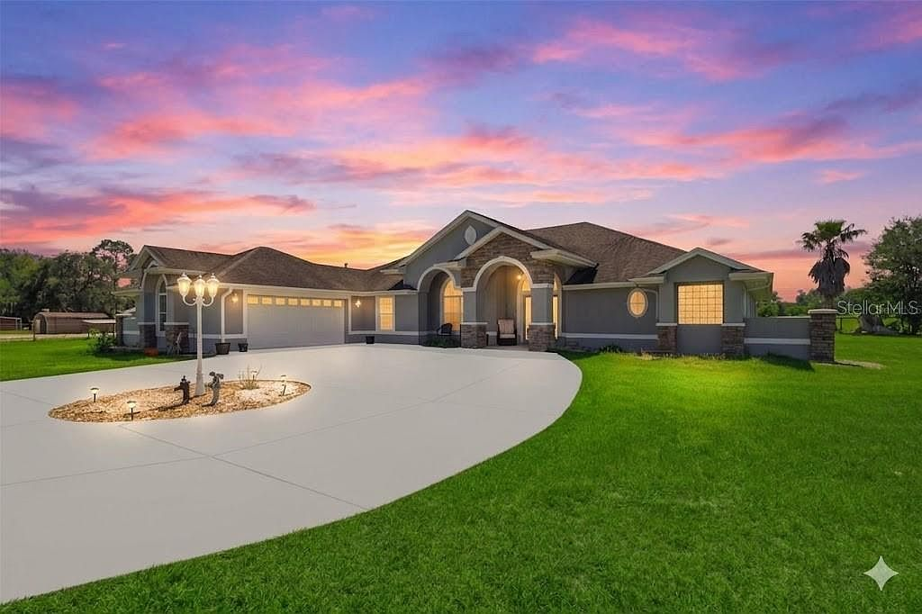Front facade at twilight with stone-accented entry archway and circular driveway