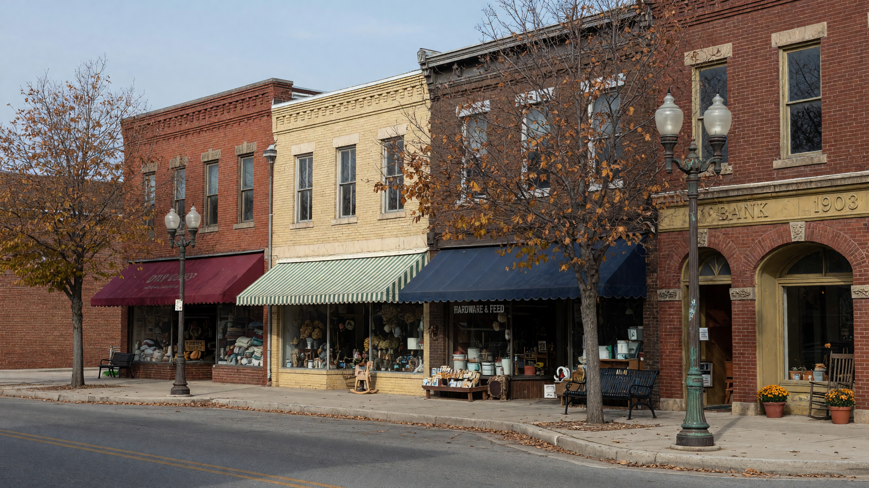 A quiet historic Main Street in a small Southern town with brick storefronts, vintage awnings, and mature trees lining the sidewalks