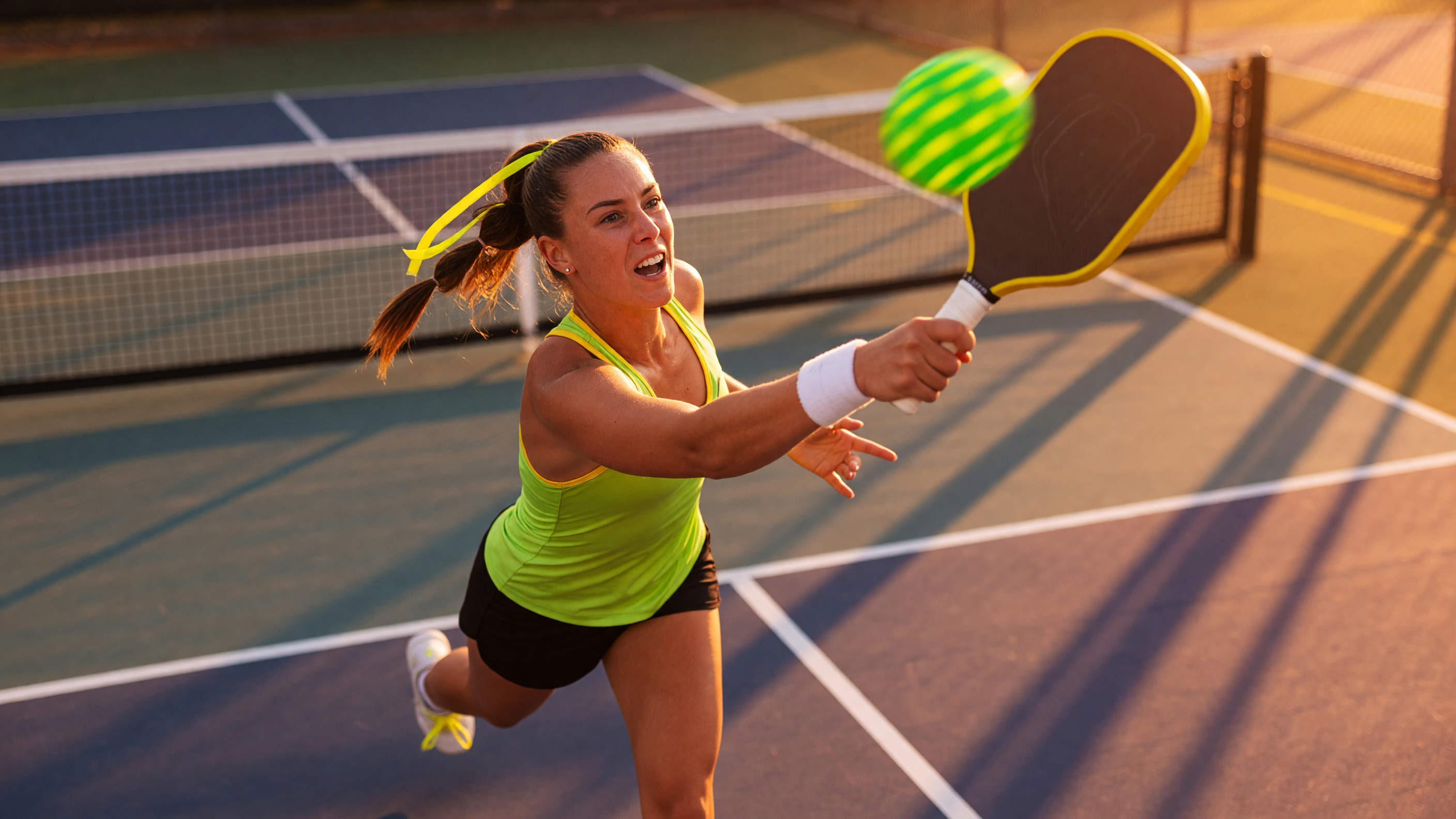 Pickleball player mid-swing on an outdoor court at golden hour