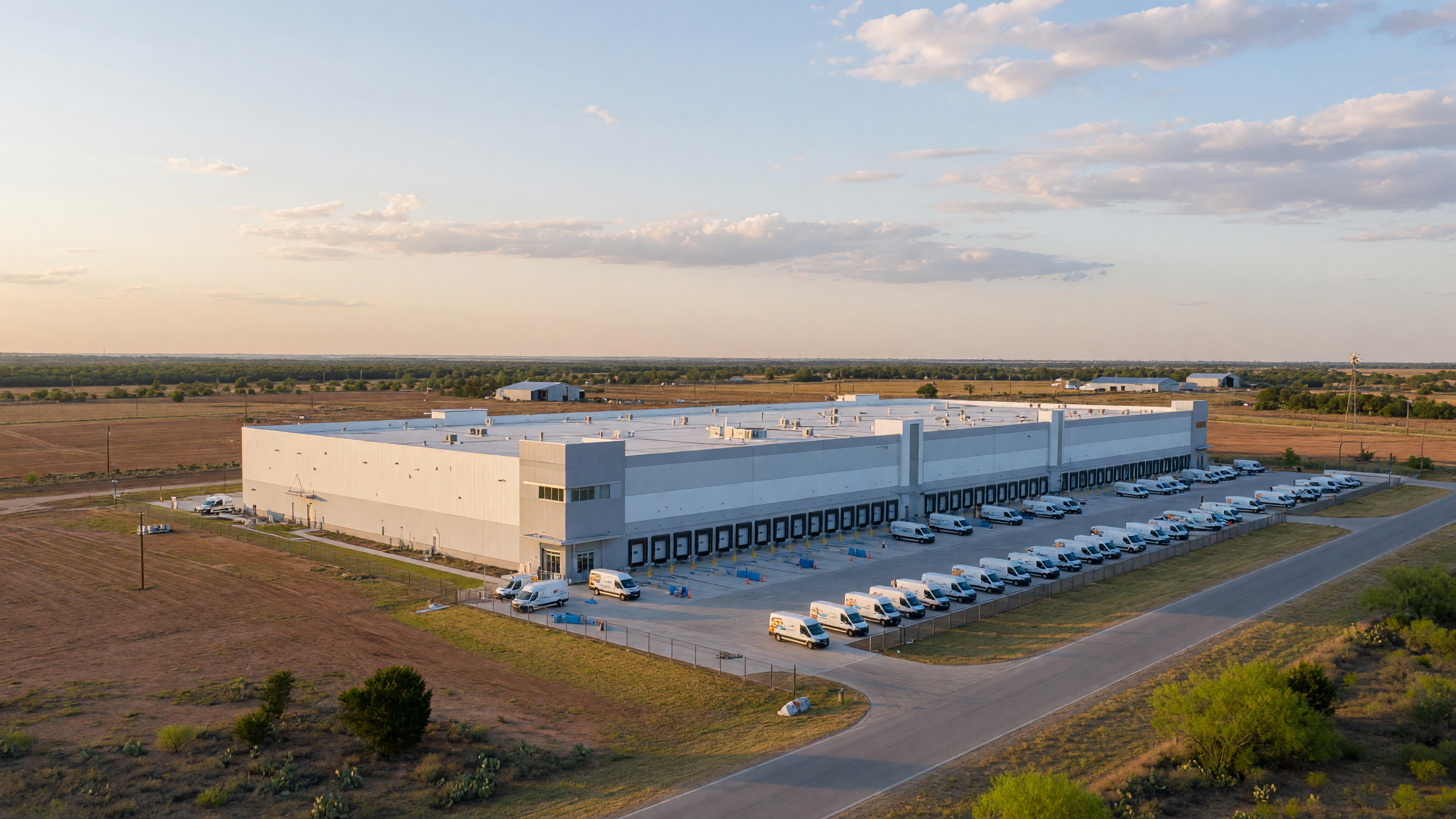 Modern Amazon delivery station warehouse facility in rural Texas with delivery vans and loading areas