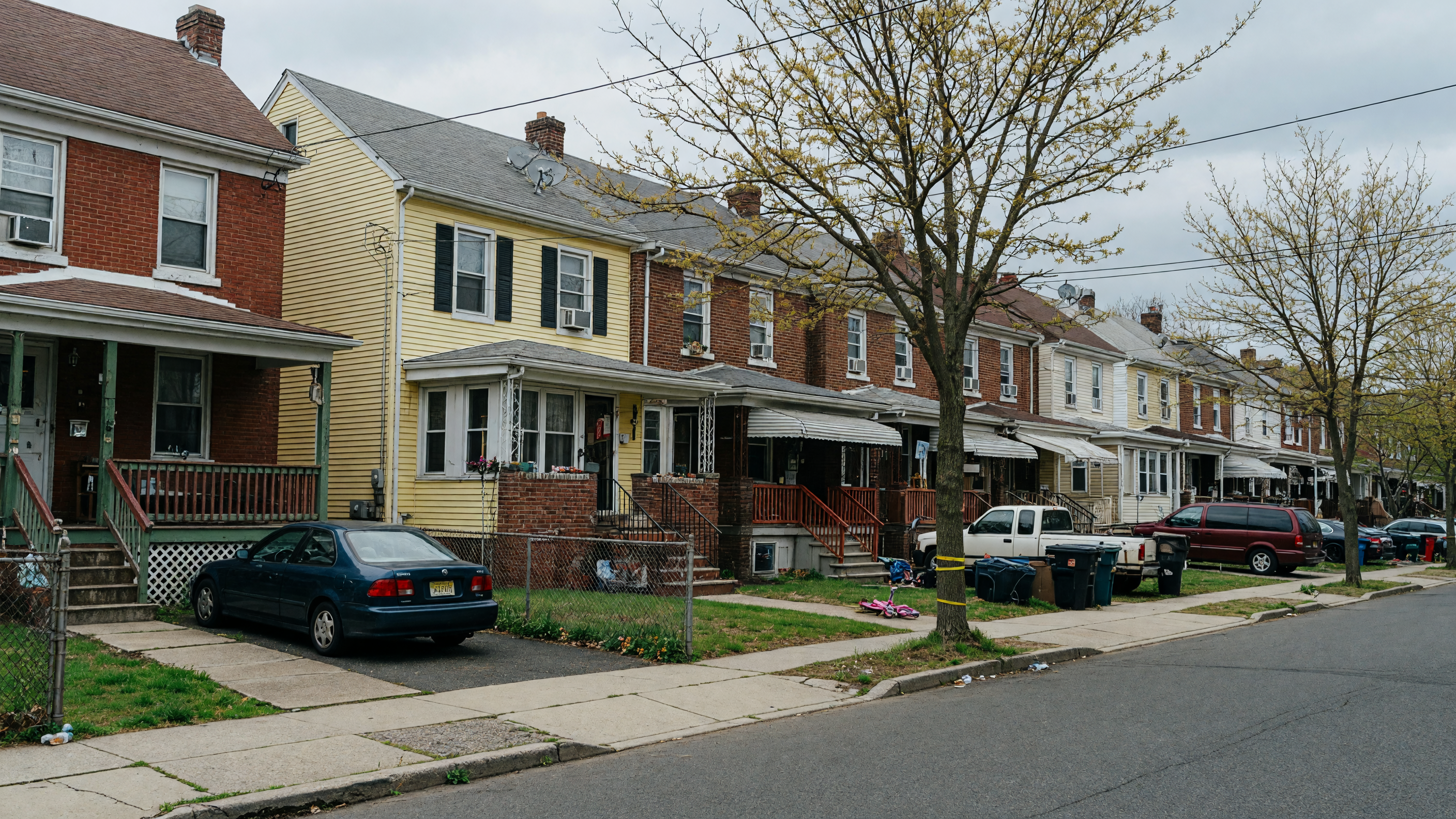 Row homes and duplex houses lining a residential street in Passaic, New Jersey on an overcast afternoon