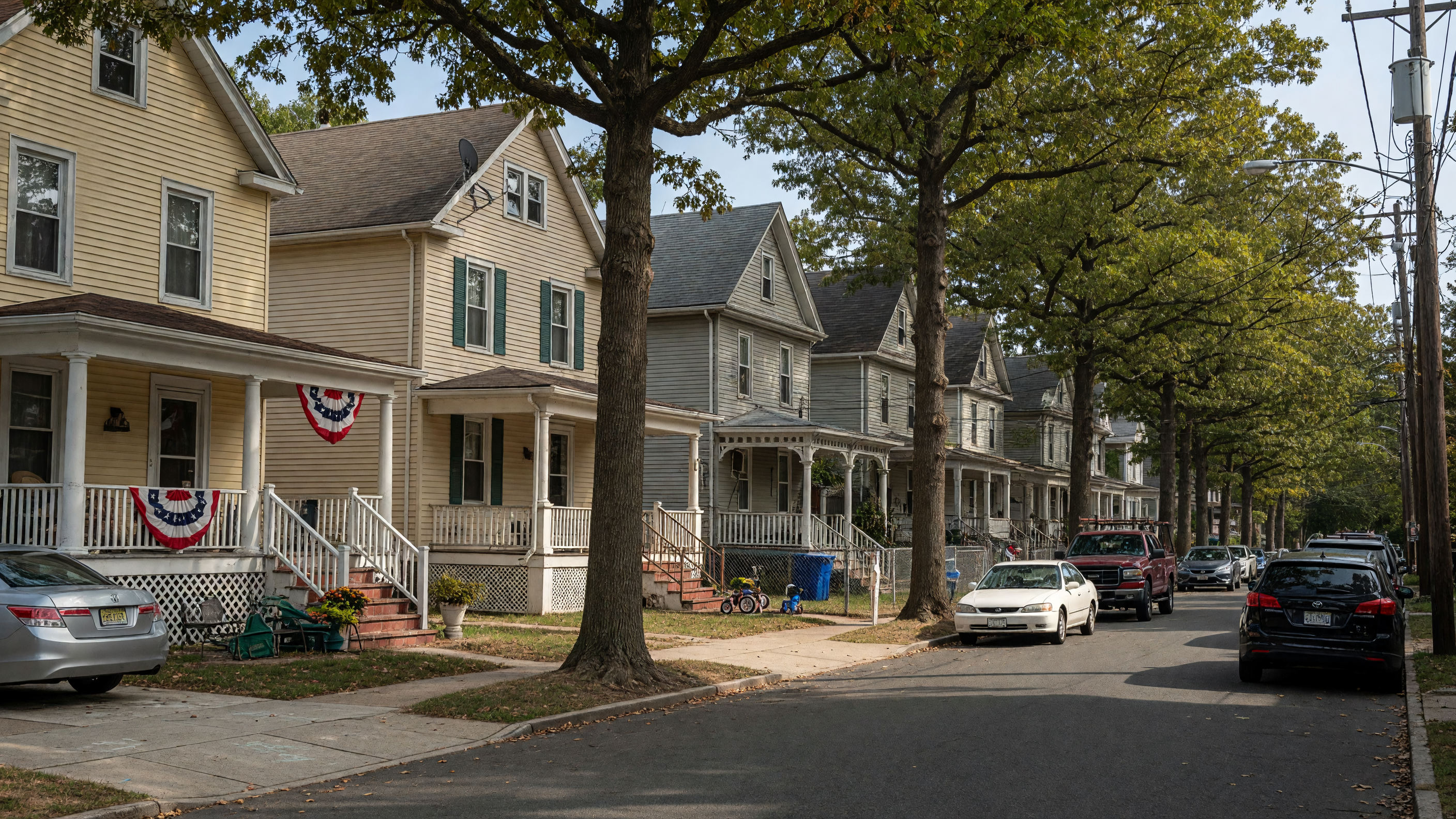 Residential street in Clifton, New Jersey with multi-family homes and mature trees along a quiet neighborhood block