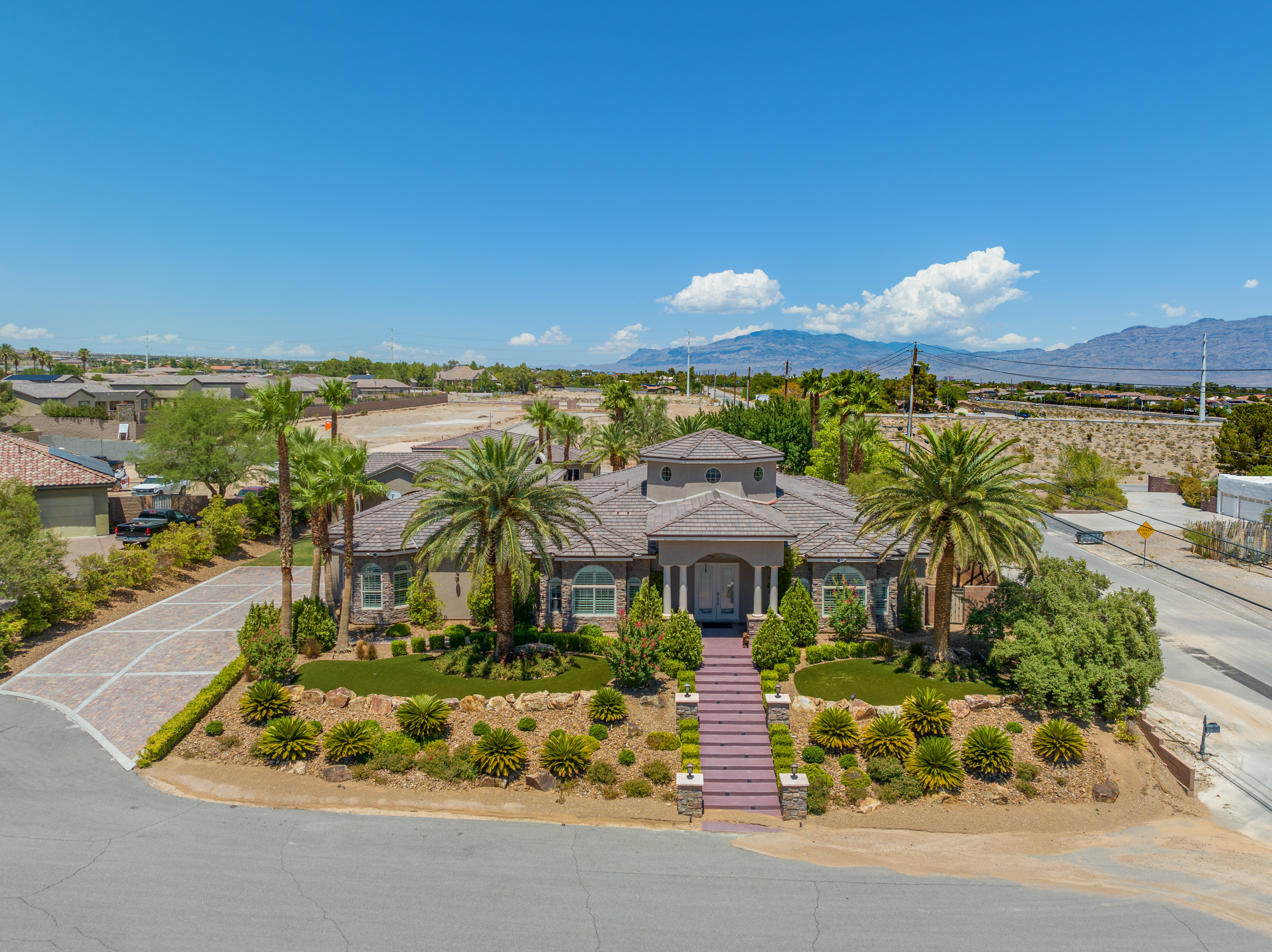 High-angle drone view of a desert-style Las Vegas suburban home with palm trees and mountain backdrop