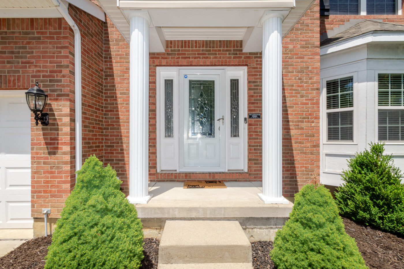 Front entry with white columns, decorative glass door, and concrete steps