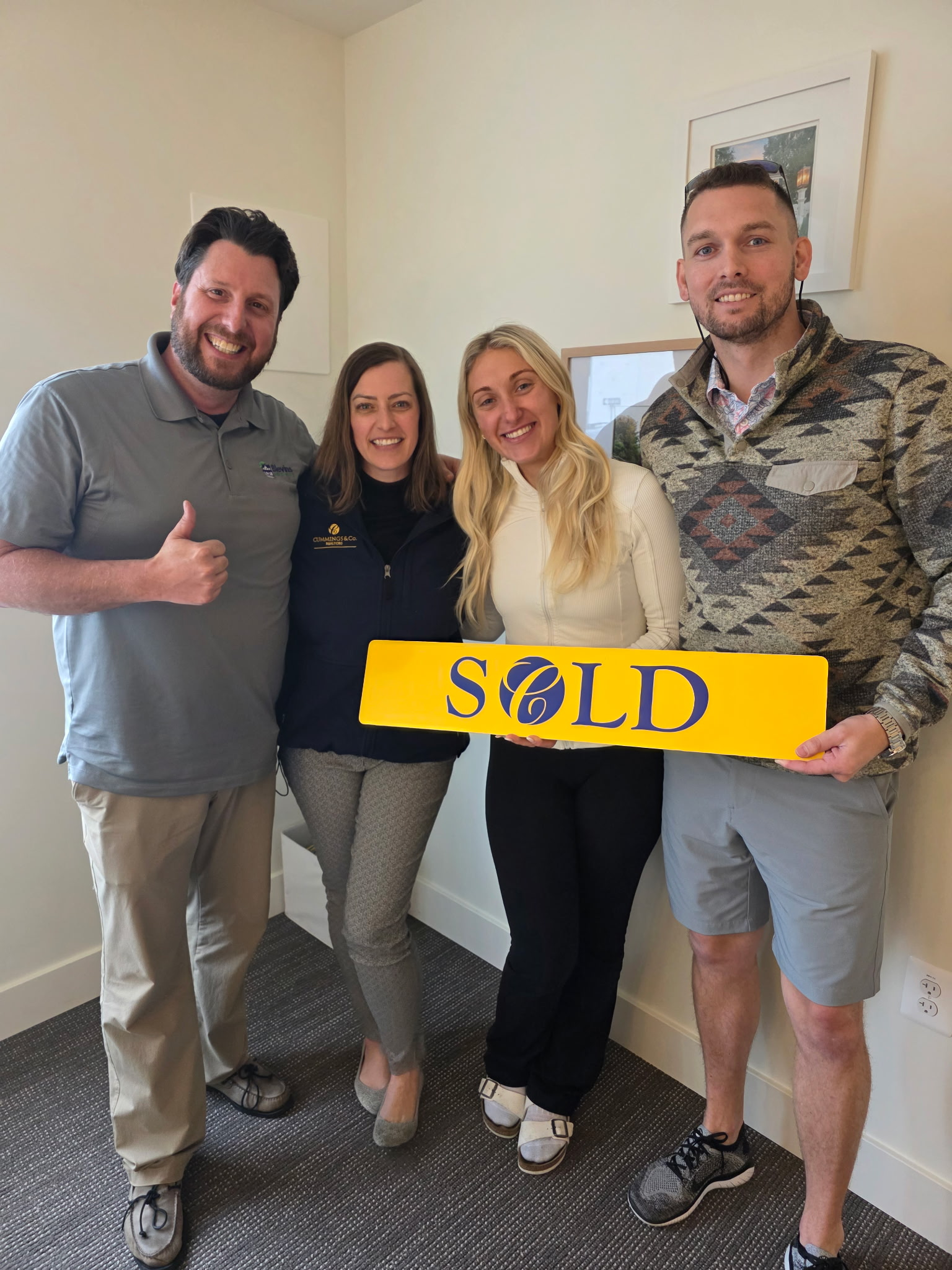 Group of people including a woman holding a yellow SOLD sign