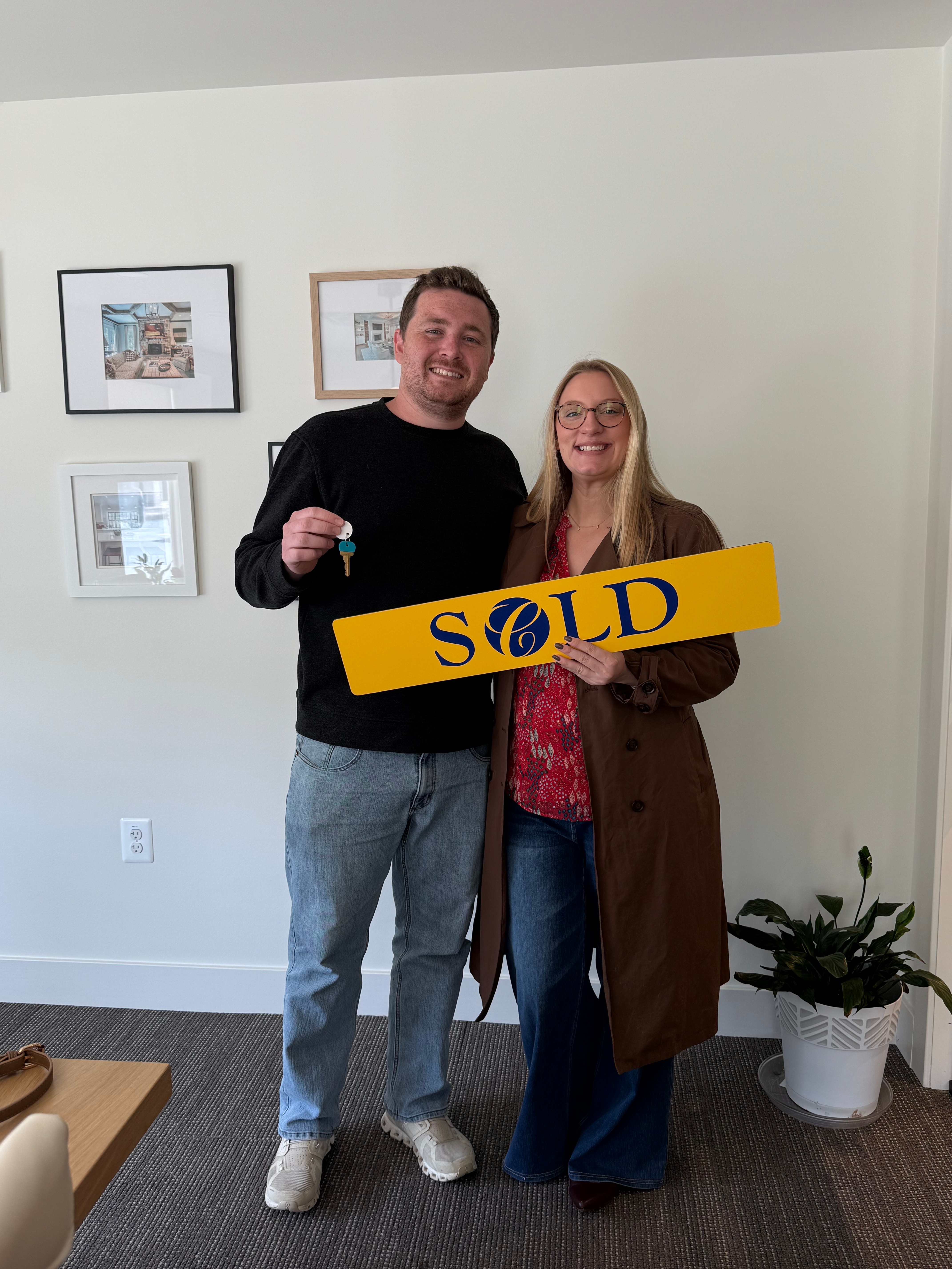 Nikki standing next to a happy client holding a house key and Sold sign