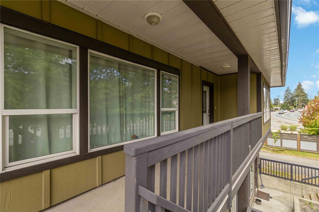 Covered upper-level front balcony with olive-green vertical siding and grey wooden picket railing