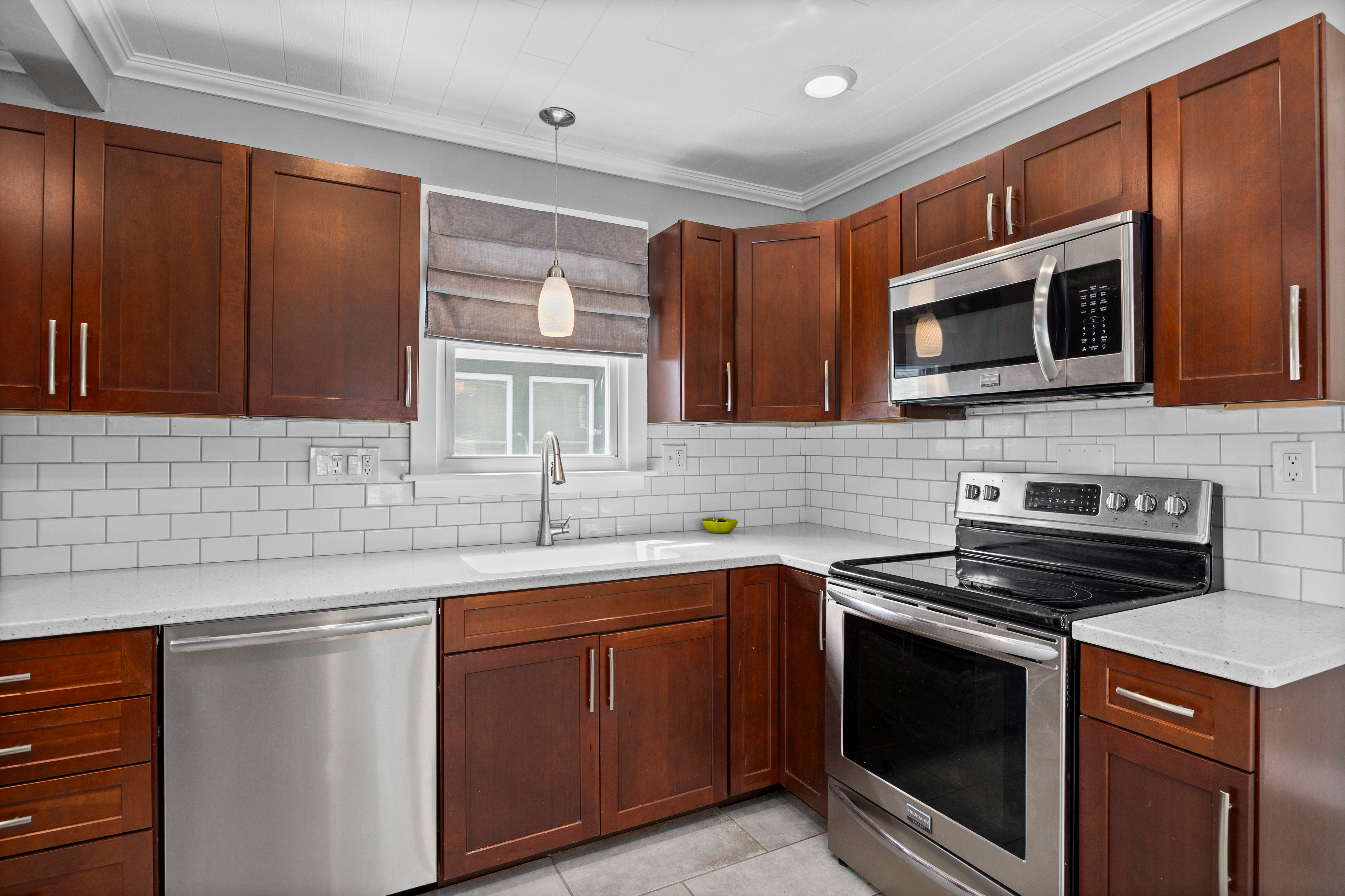 Updated kitchen with stained wood shaker cabinets, white quartz countertops, and subway tile.